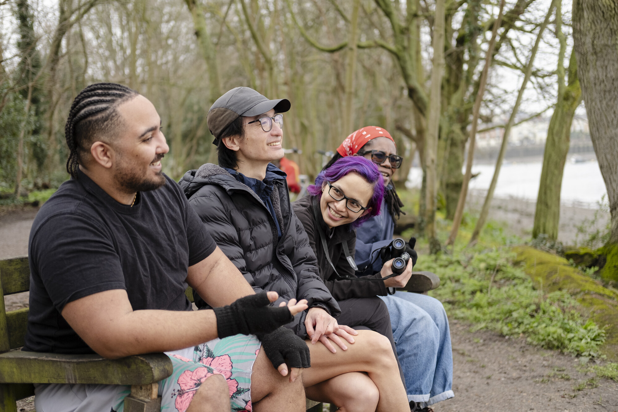 Four people sit on a bench along the side of the Thames Path