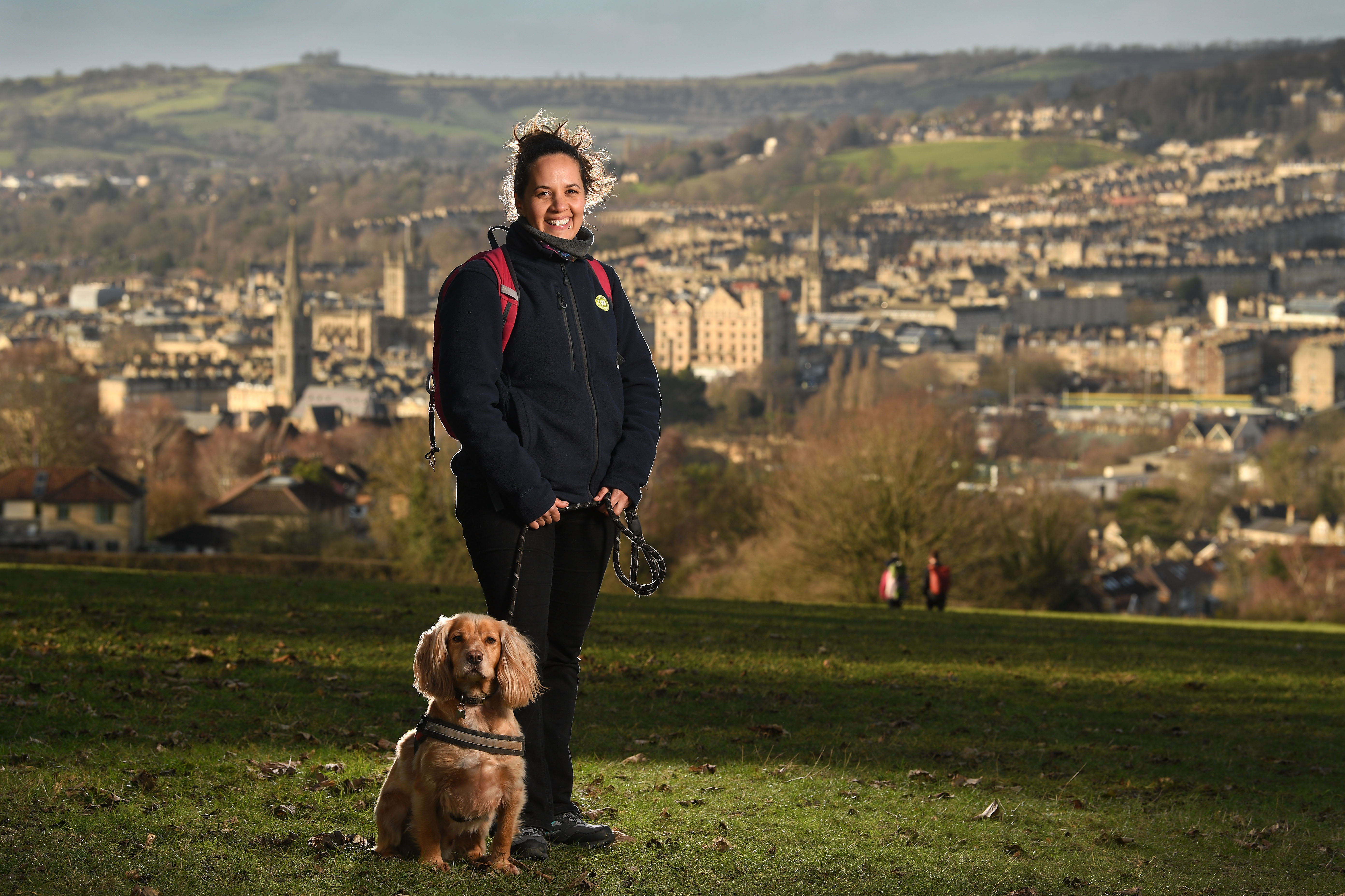 Nicole Daw the blog author and Access and Volunteers Officer at Cotswolds National Landscape stands with her dog on a hill overlooking Bath where the Cotswolds Way starts