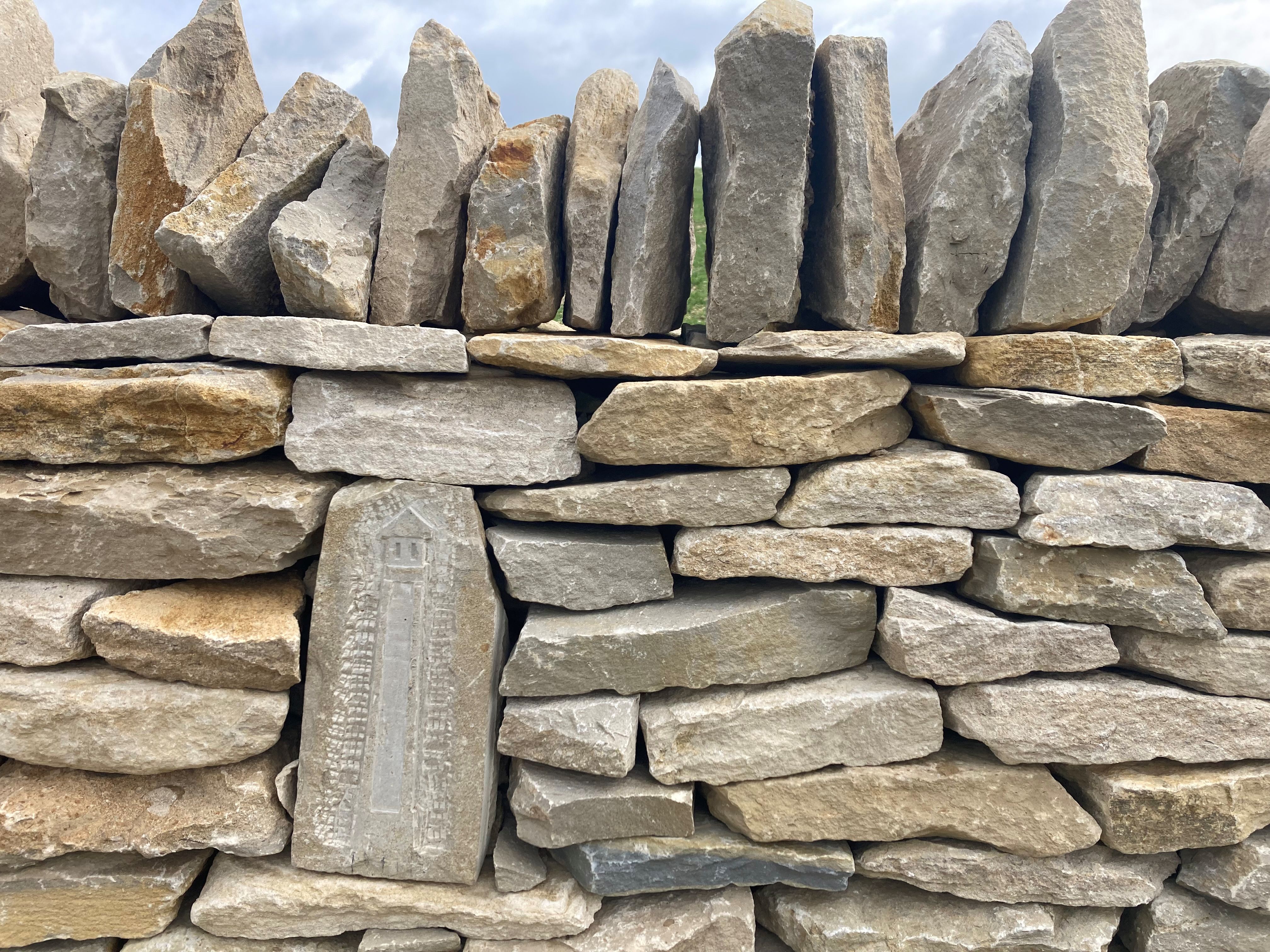 A section of dry stone wall on the Leckhampton and Charlton Kings Accessible Loop, with one of the stones having an engraving of the Tyndale monument