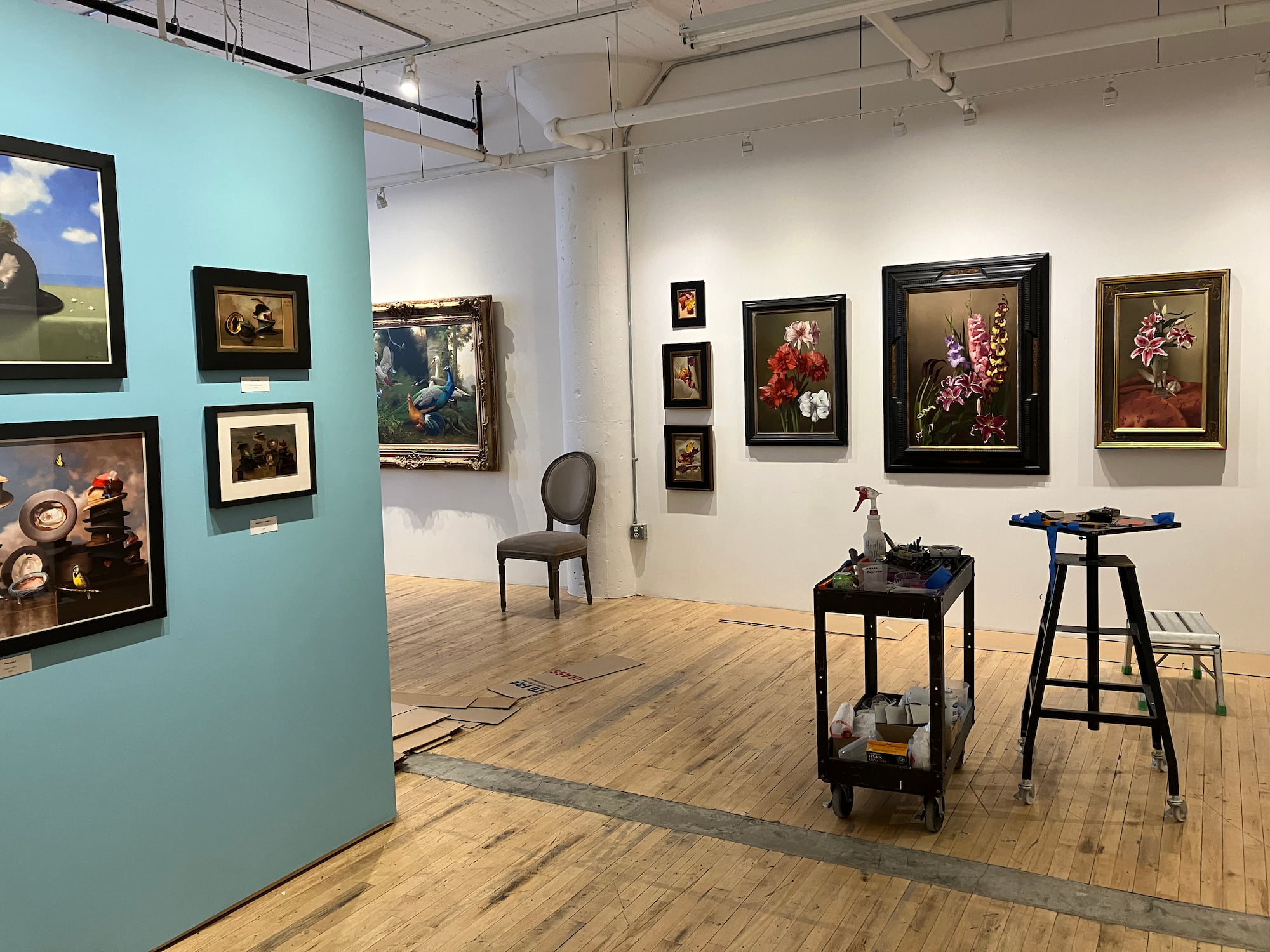 A tools cart sits in front of paintings on the walls in a gallery space.