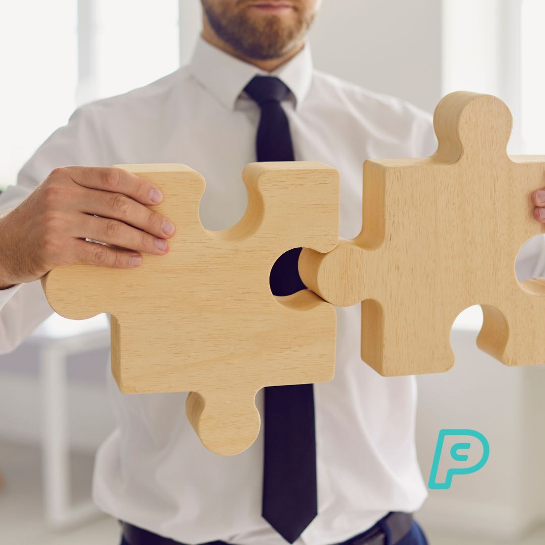 A man in a white shirt and tie holding two jigsaw pieces together, demonstrating how payroll software fit with other business solutions