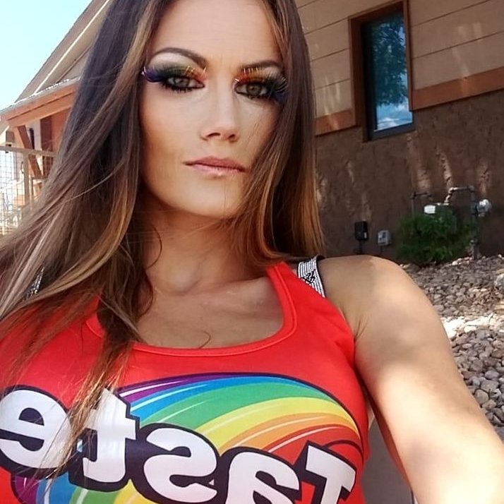 Woman with long brown hair wearing vibrant rainbow eye makeup and a red tank top with a rainbow graphic.