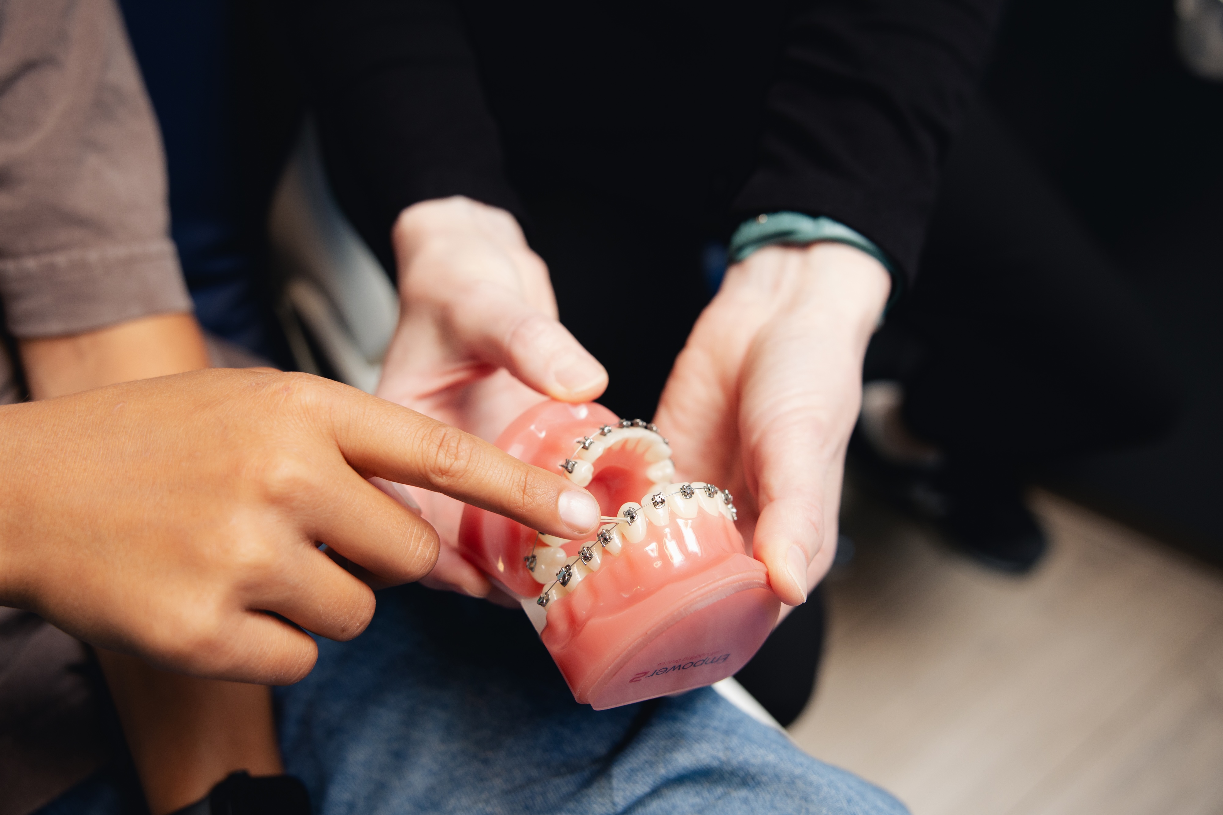 A 3D model of a set of teeth with braces is being held by the orthodontist while the child points at it.