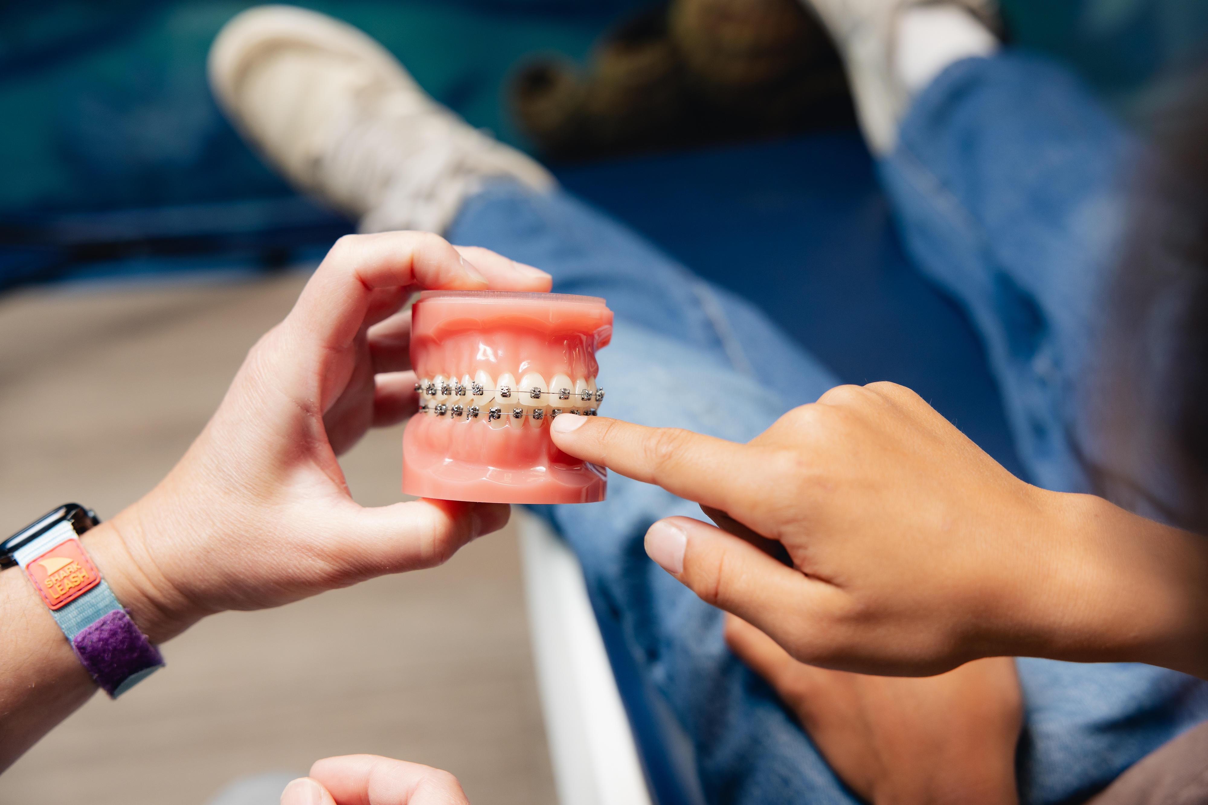 The orthodontist is holding up a 3D model of a set up teeth with braes while the child is pointing at the braces.