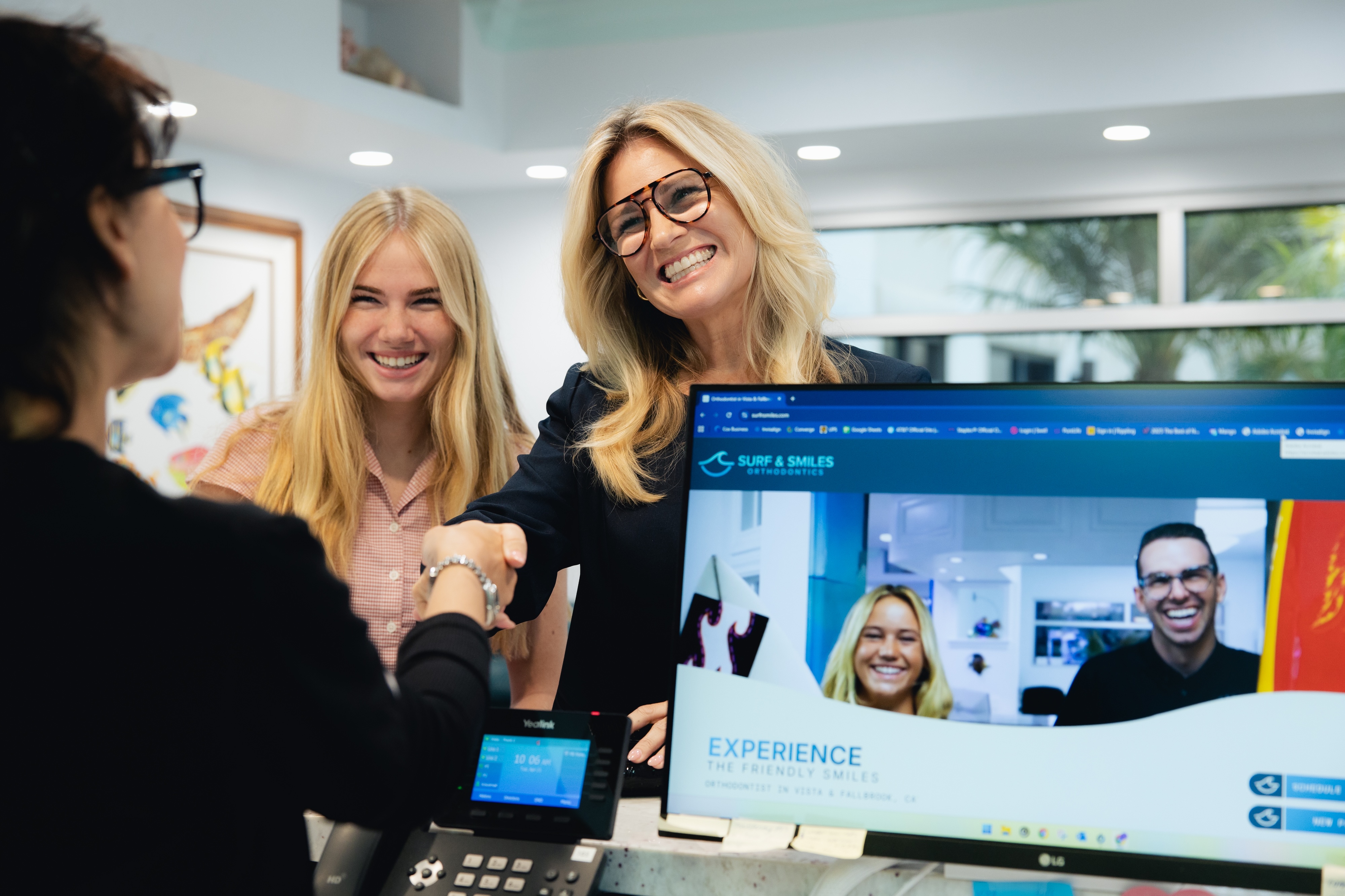 A mom and her teenage daughter are standing at the reception desk and the mom is shaking hands with the receptionist after paying for her daughters new smile. 
