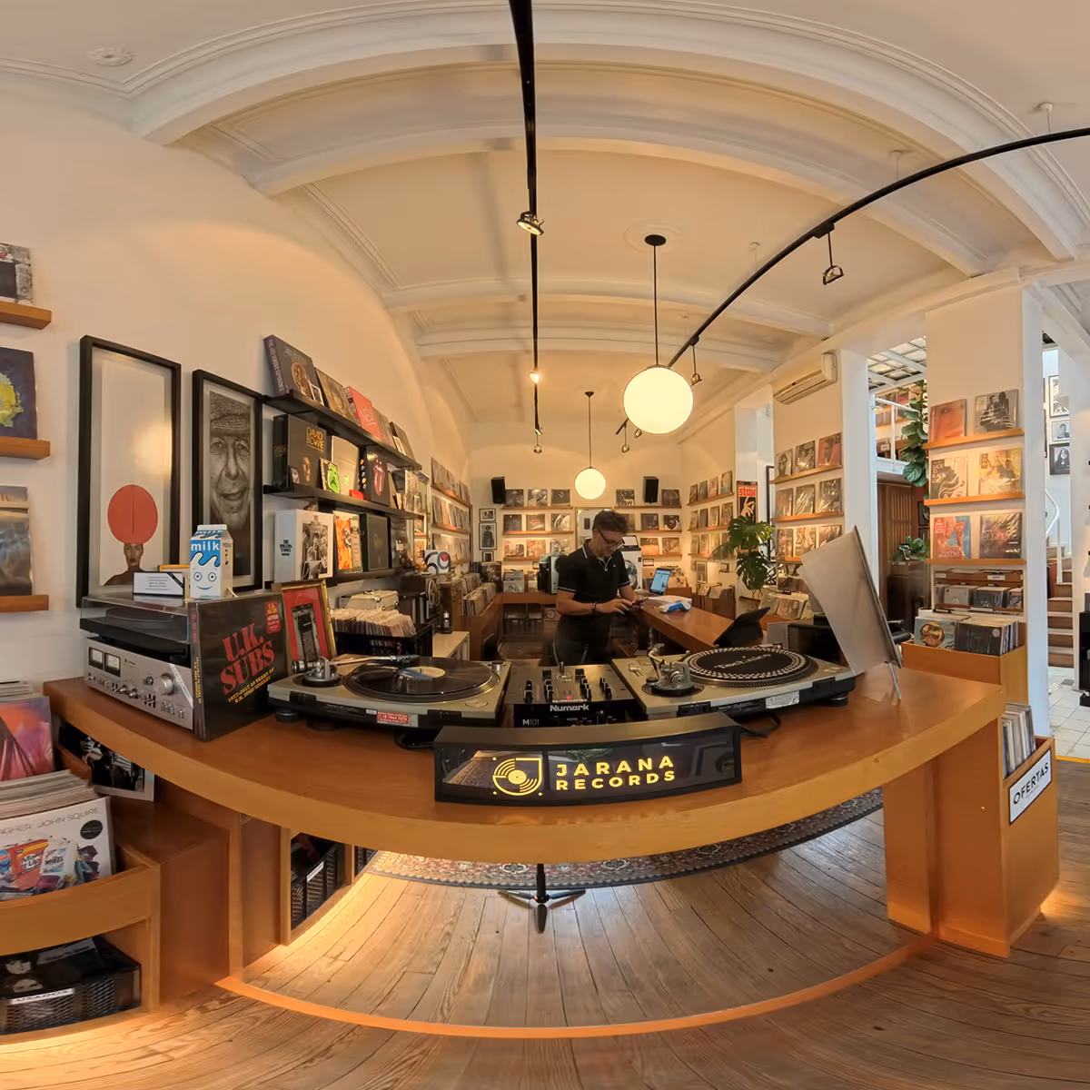 Interior of Jarana Records store featuring turntables on a wooden counter and a person working behind it surrounded by vinyl records on shelves.