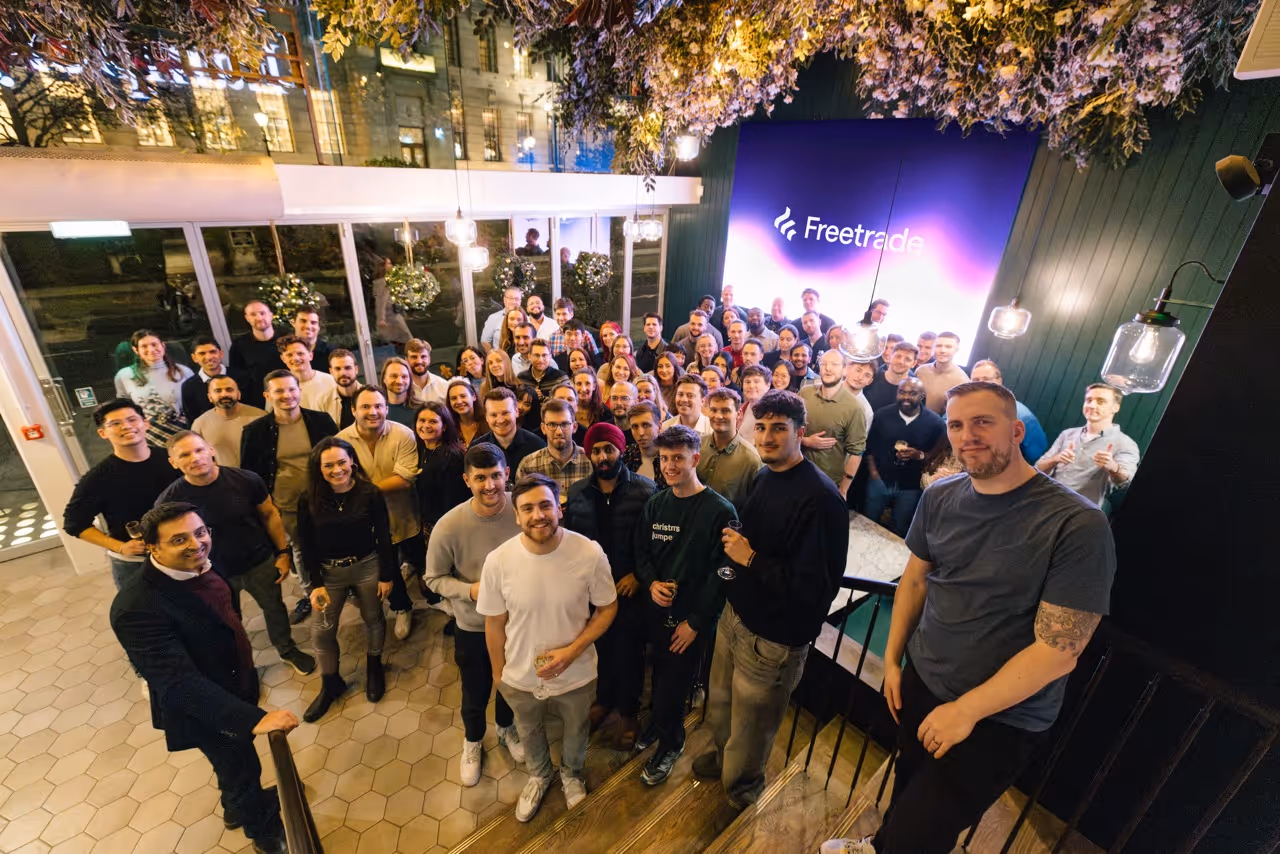Large group of people posing and smiling indoors under decorative lights near a Freetrade sign.