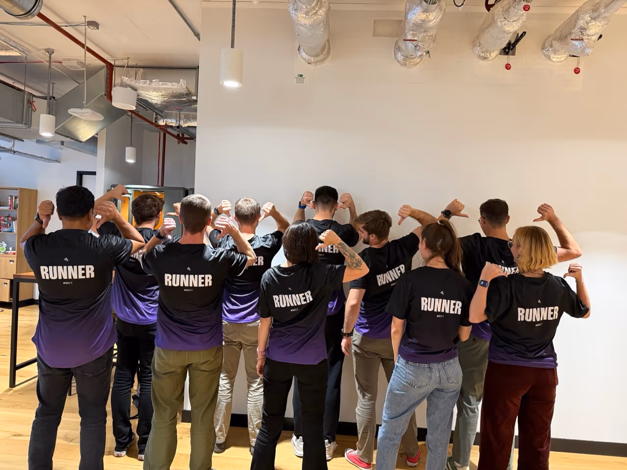 Group of people indoors wearing black and purple shirts labeled RUNNER on the back, showing thumbs down.