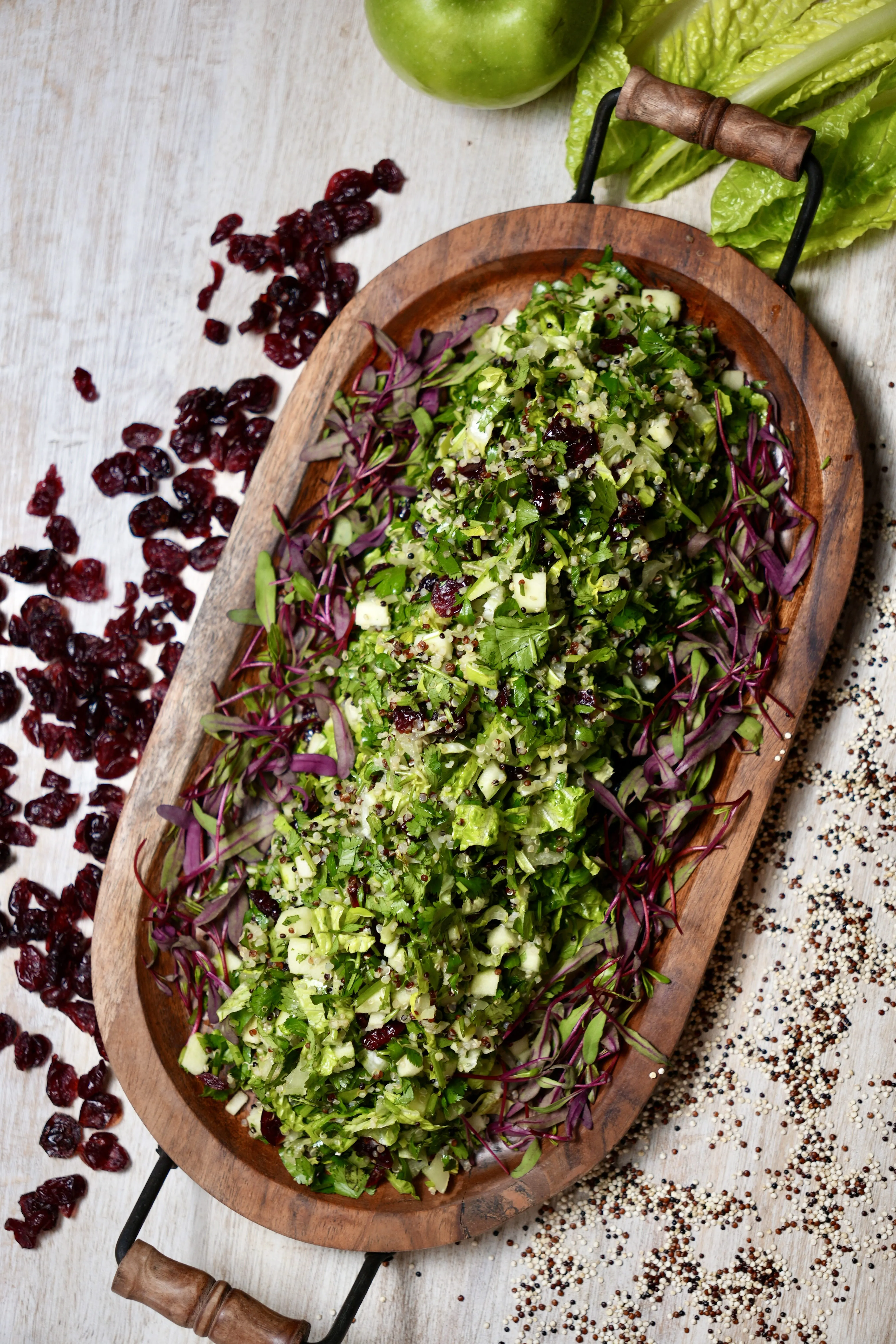 Chopped salad with quinoa, fresh herbs and cranberries on a carved wooden board