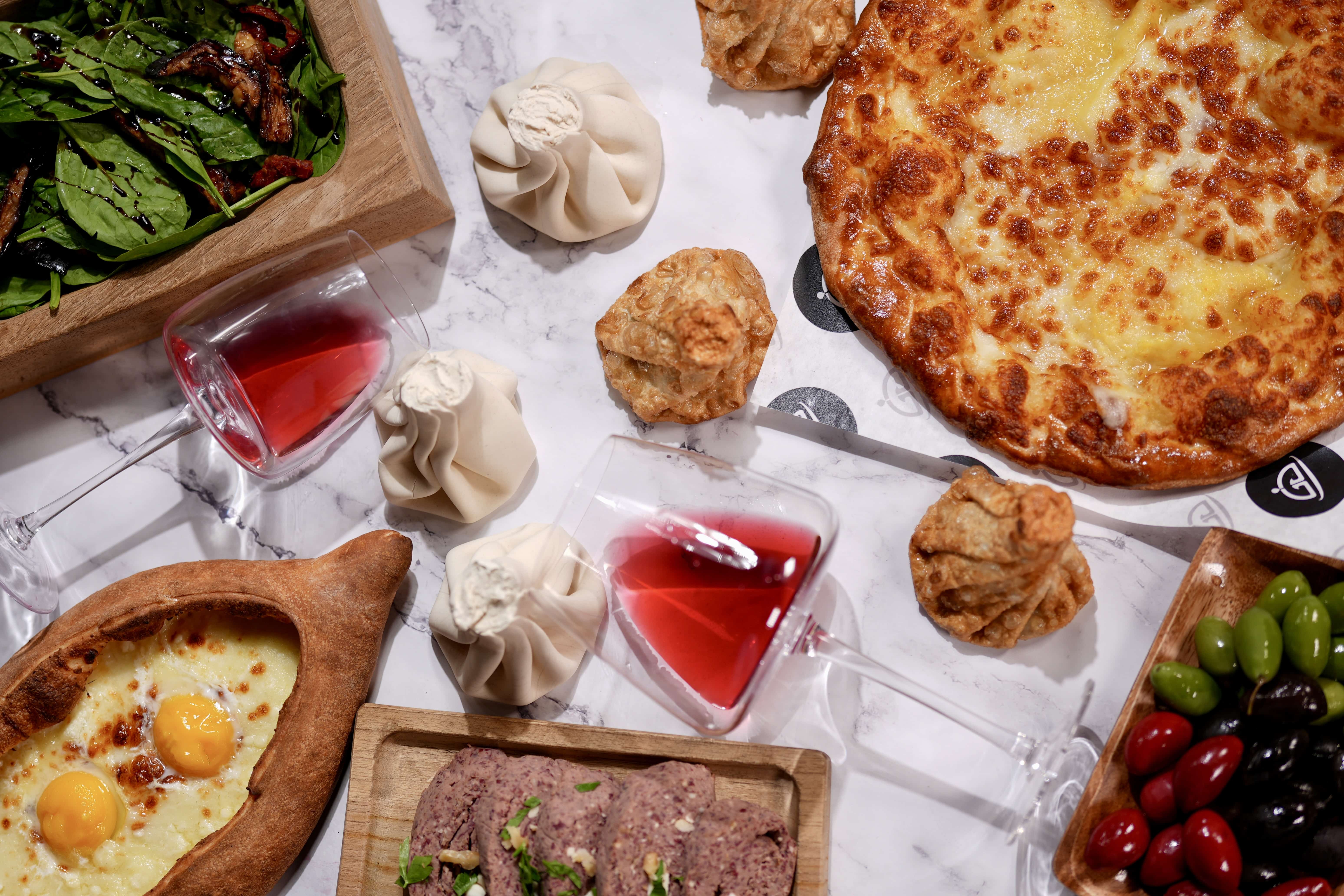 A laid table of Armenian and Georgian dishes: khinkali, khachapuri, ajarski, salad and olives