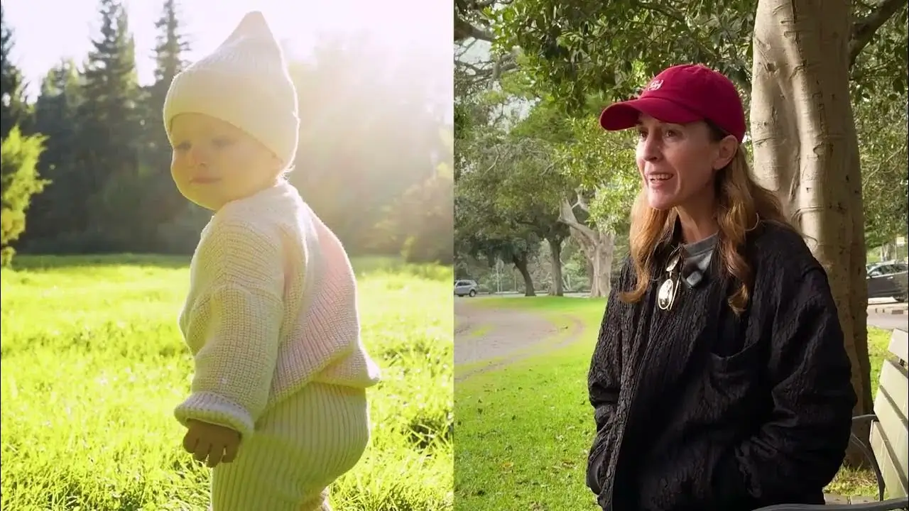 Side views of a toddler in warm clothes outdoors and a woman in a red cap beside a tree in a park.