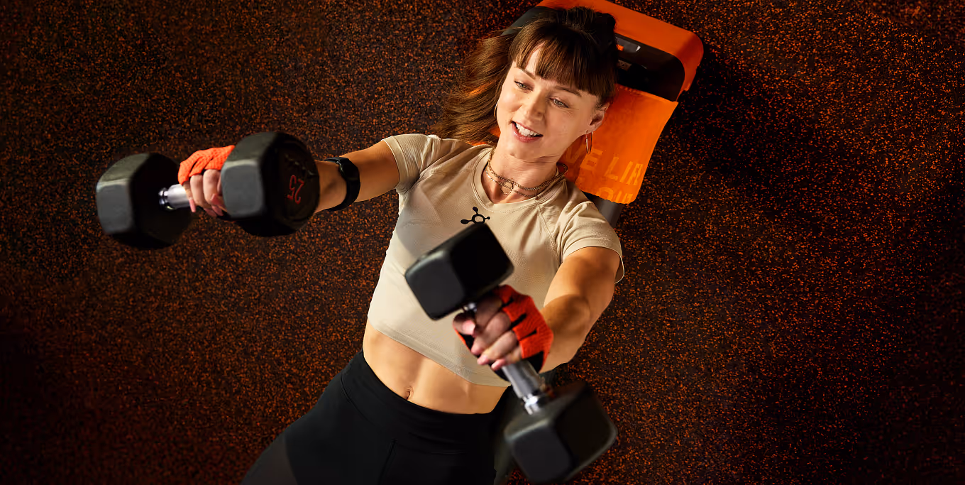 Woman in her mid-30s bench pressing dumbbells.