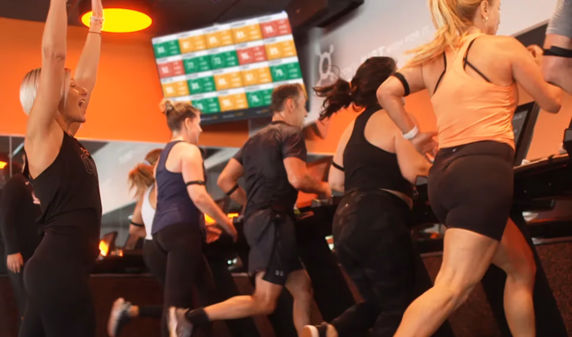 Coach leading a tread class as participants run on treadmills.
