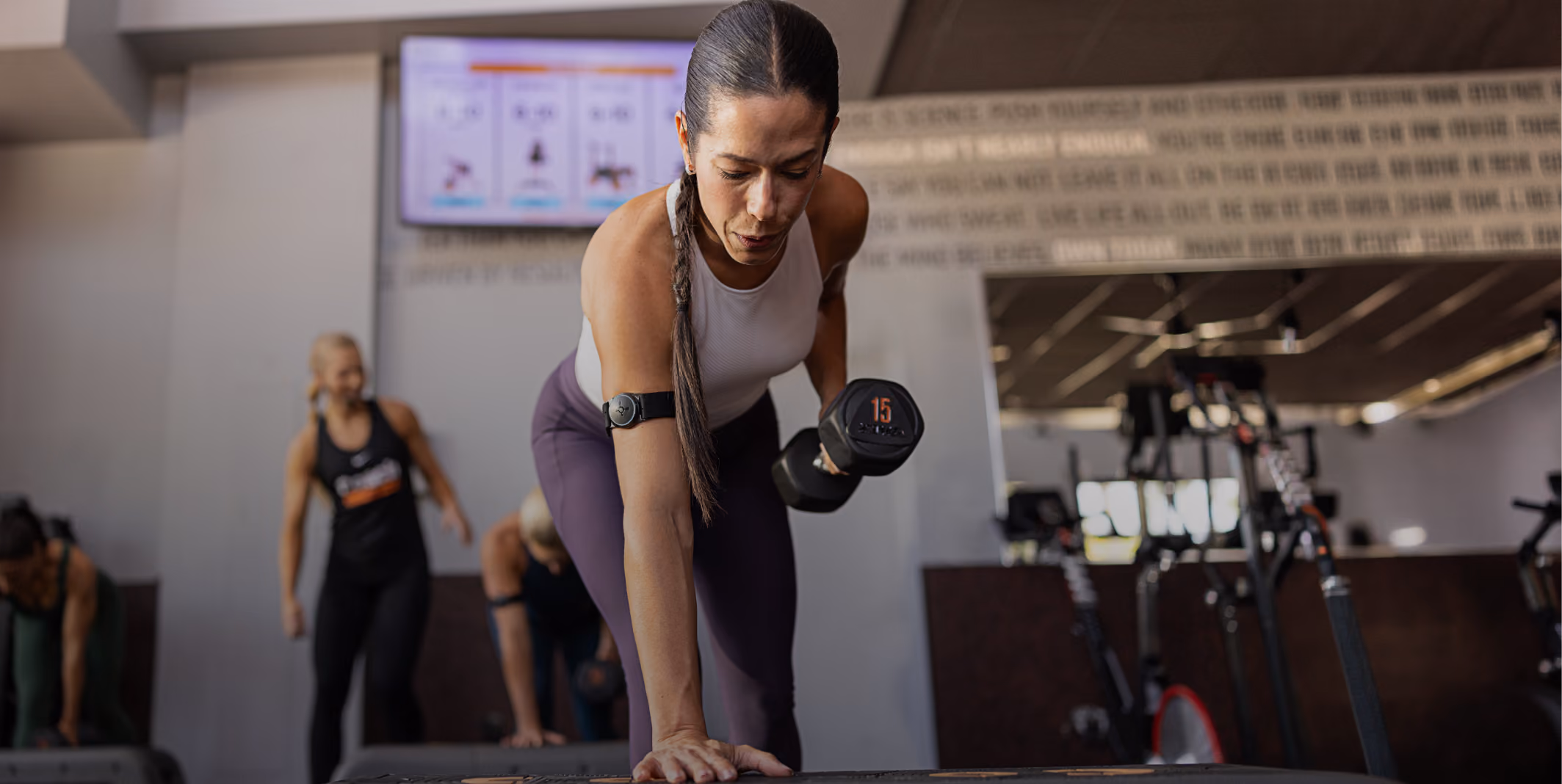 Woman in a gym lifting a 15-pound dumbbell while supporting herself on a platform.