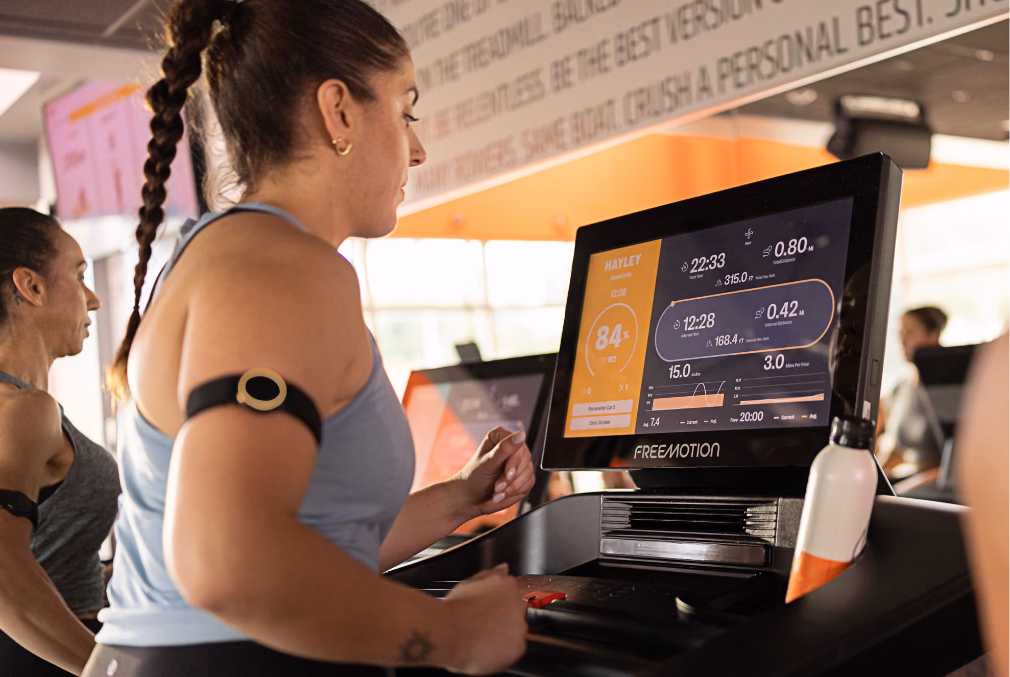 Woman running on treadmill with a heart rate monitor and fitness stats shown on the console screen.