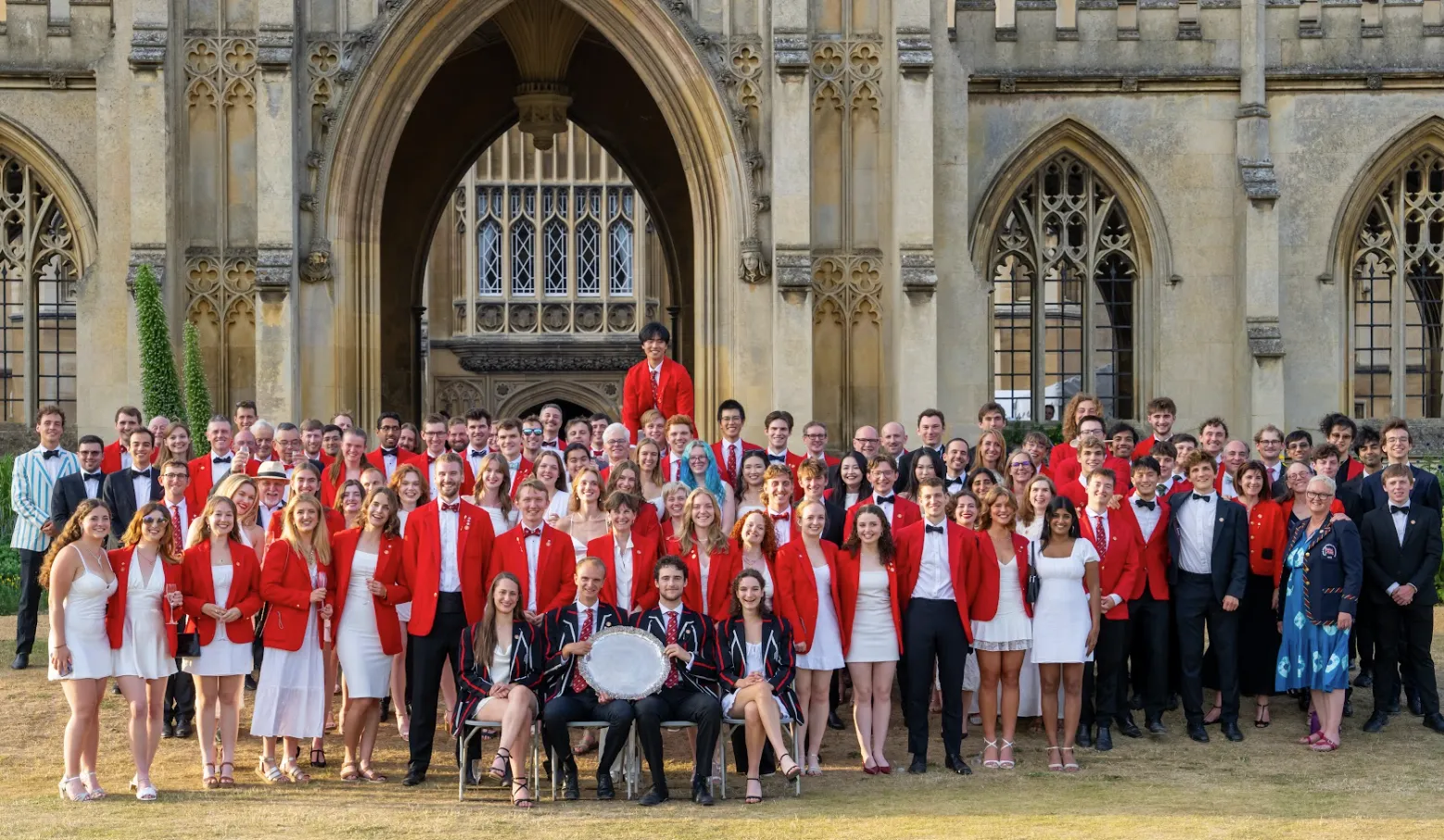 Lady Margaret Boat Club members with the 2025 Headship silver plate in front of New Court building at St John's College, wearing their trademark red jackets