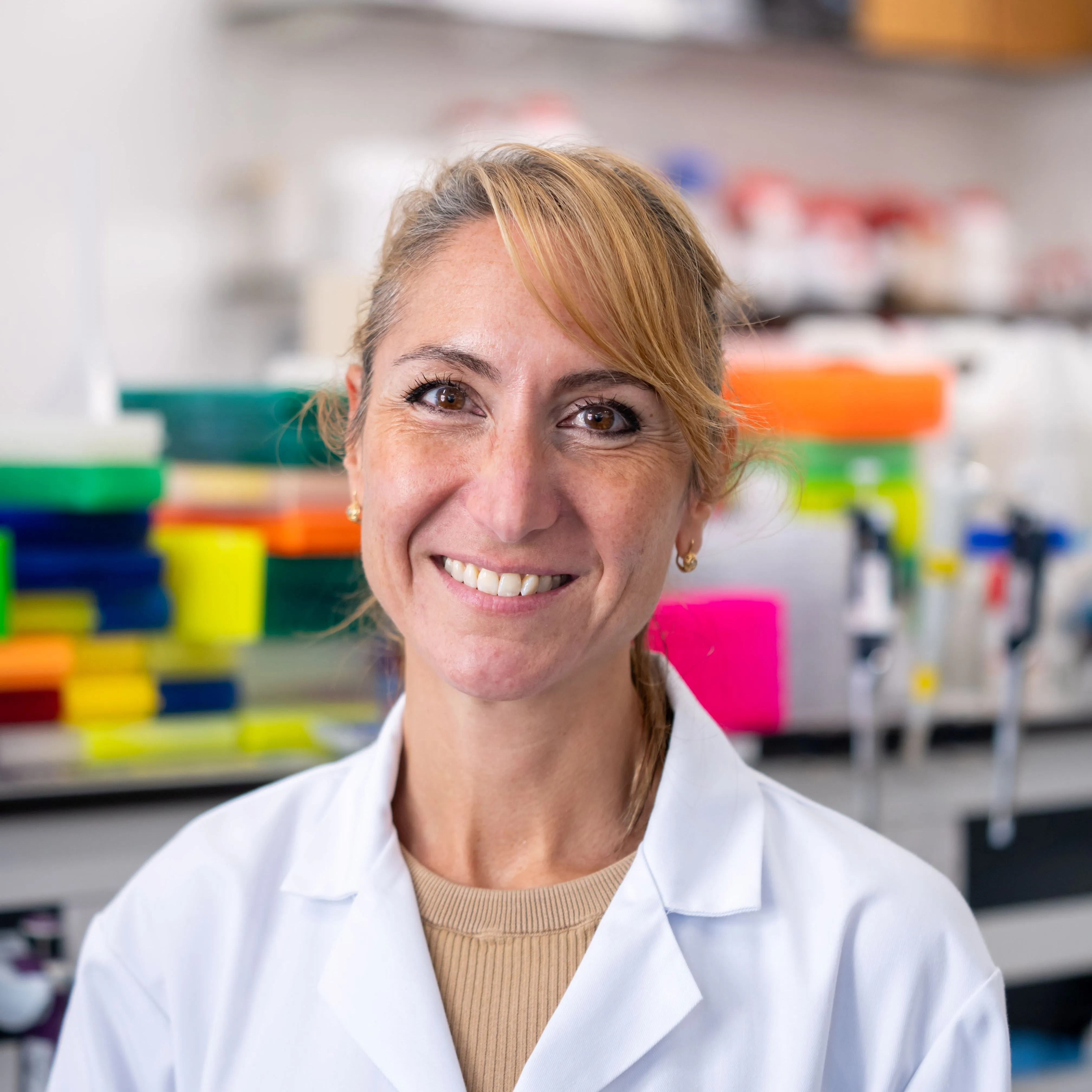 A photograph of Professor Amanda Sferruzzi-Perri smiling, wearing a white lab coat in a laboratory