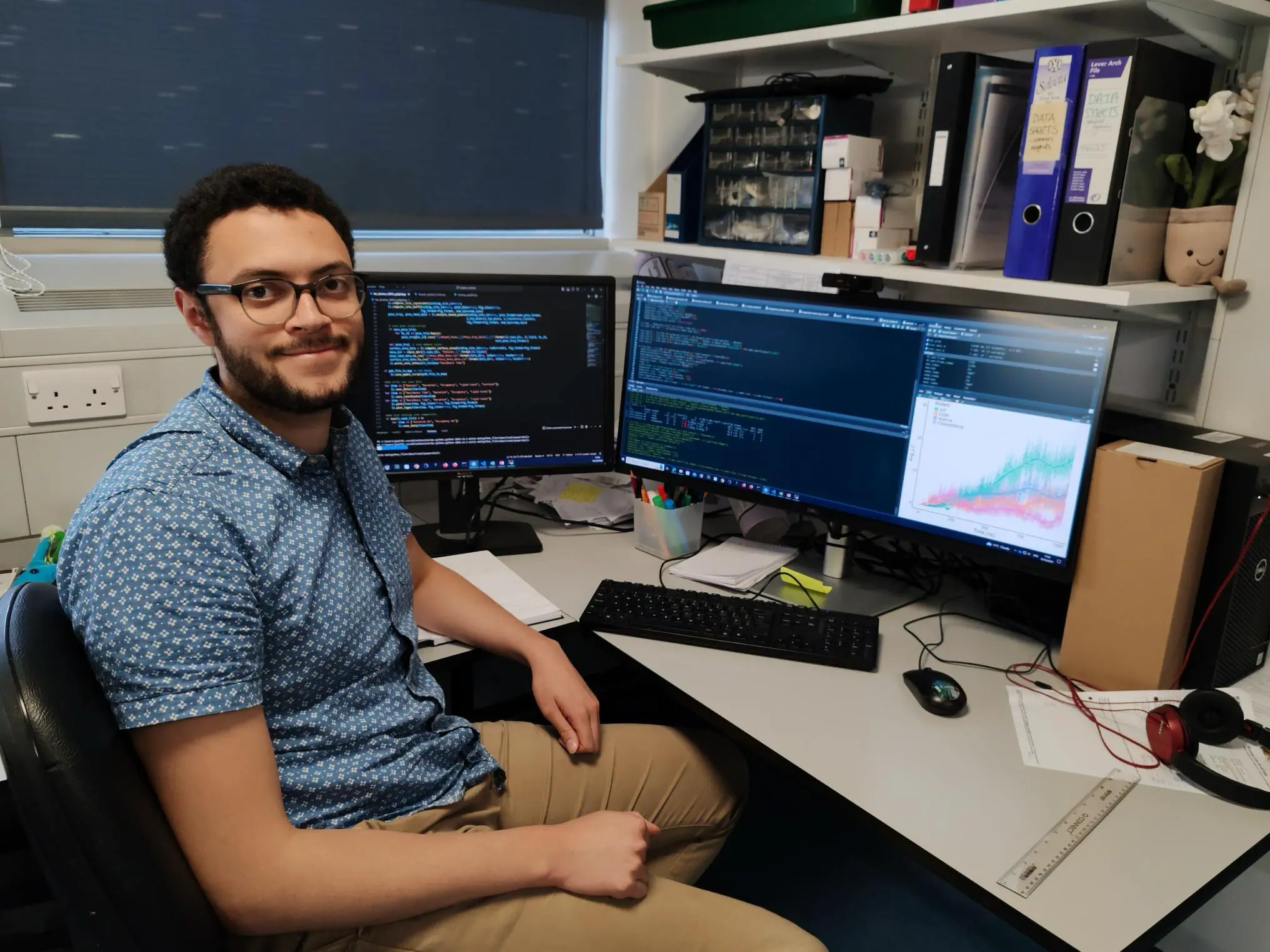 A photograph of Jack Welland, a PhD researcher at St John's College, Cambridge, sitting at his computer desk, turned towards the camera and smiling