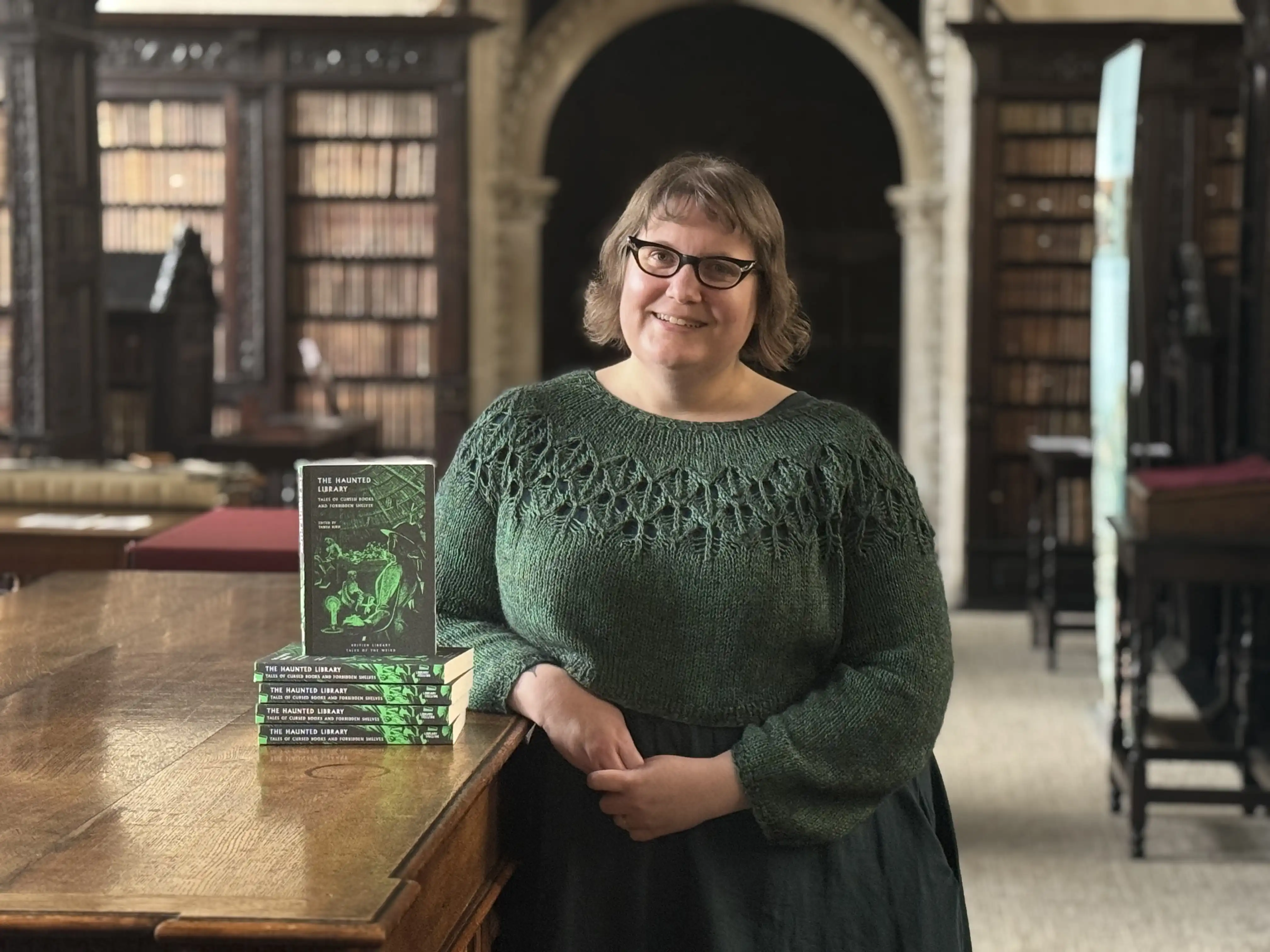St John's College Librarian Tanya Kirk leans against a cabinet in the Old Library next to a pile of her new book. The Haunted Library