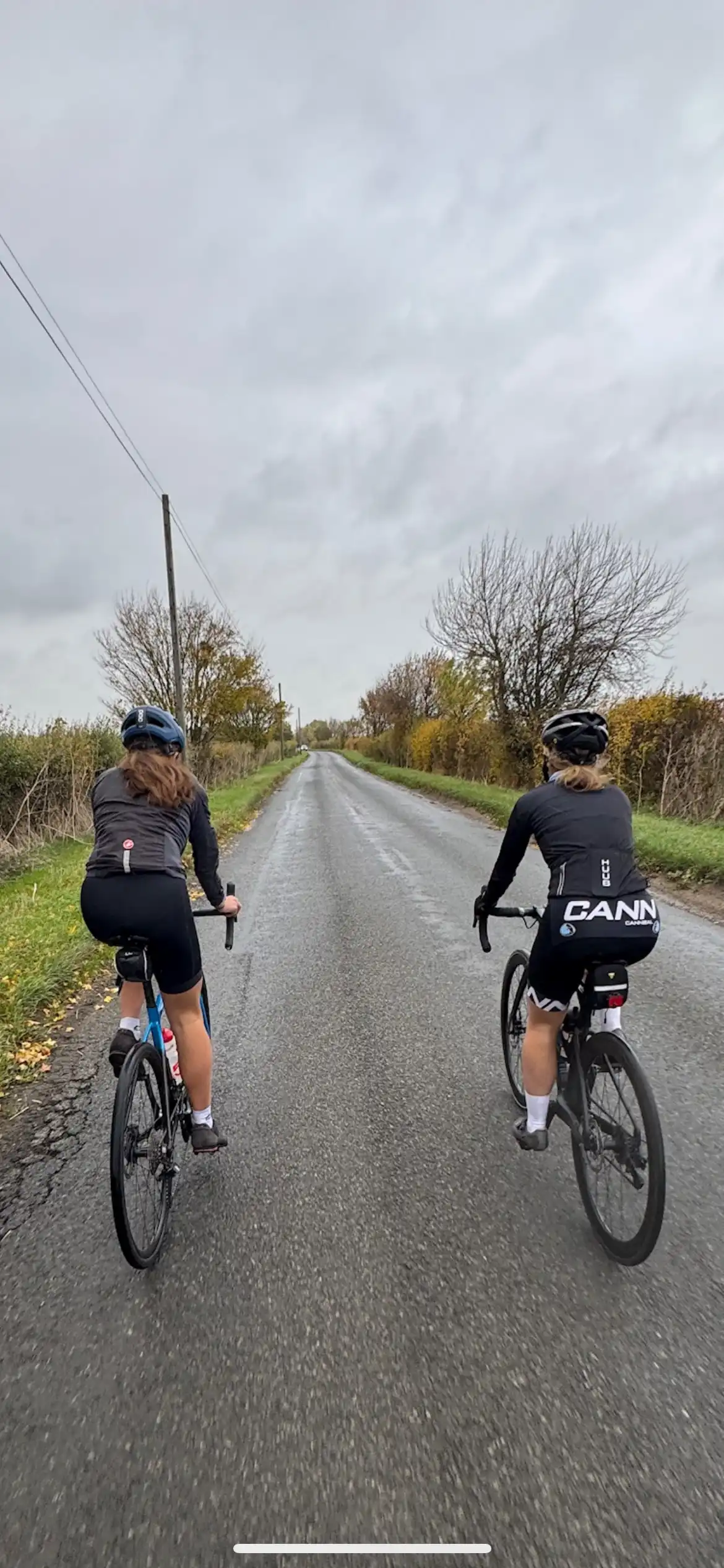View from behind of two cyclists riding along a flat country road