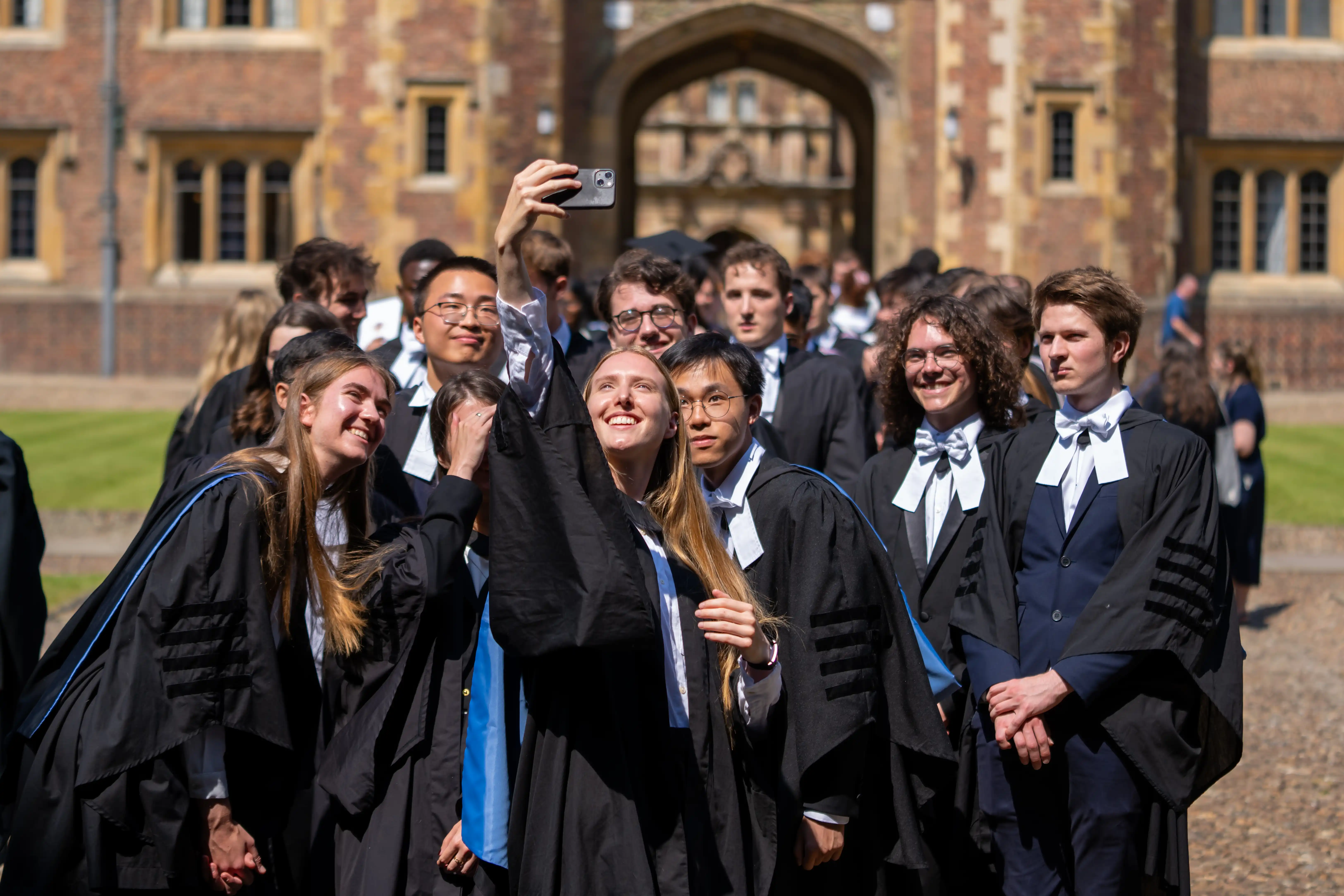 Graduating students in their black gowns are photographed posing to take a group selfie with a smartphone in Second Court, St John's College, Cambridge