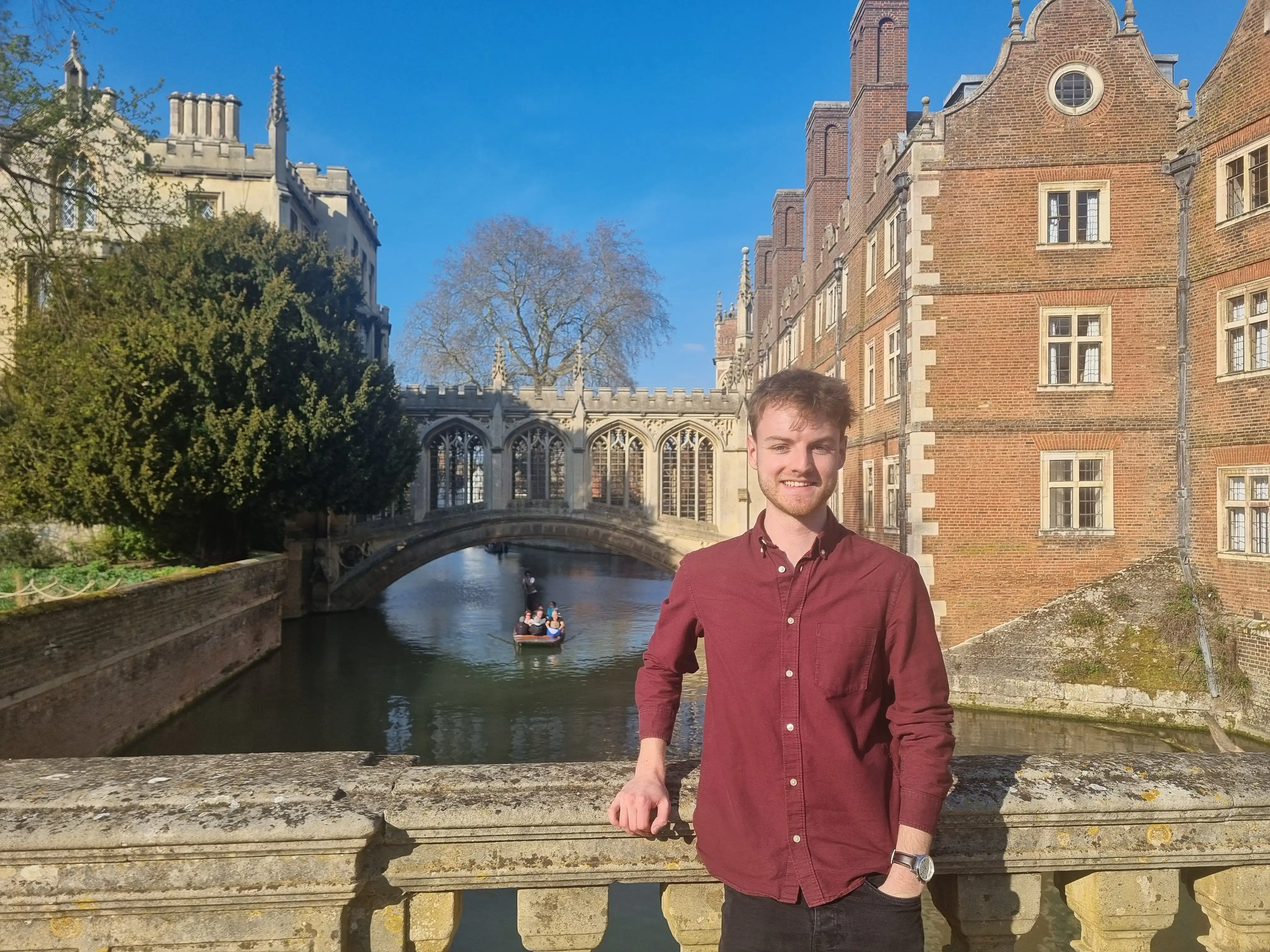 PhD student Will Duckett poses on Kitchen Bridge at St John's College, Cambridge, with the Bridge of Sighs in the background