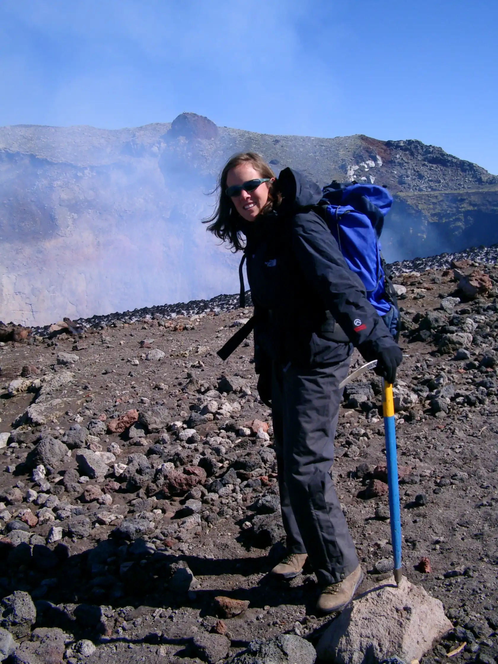 Professor Tamsin Mather stands on the summit of a volcano as smoke plumes rise behind her