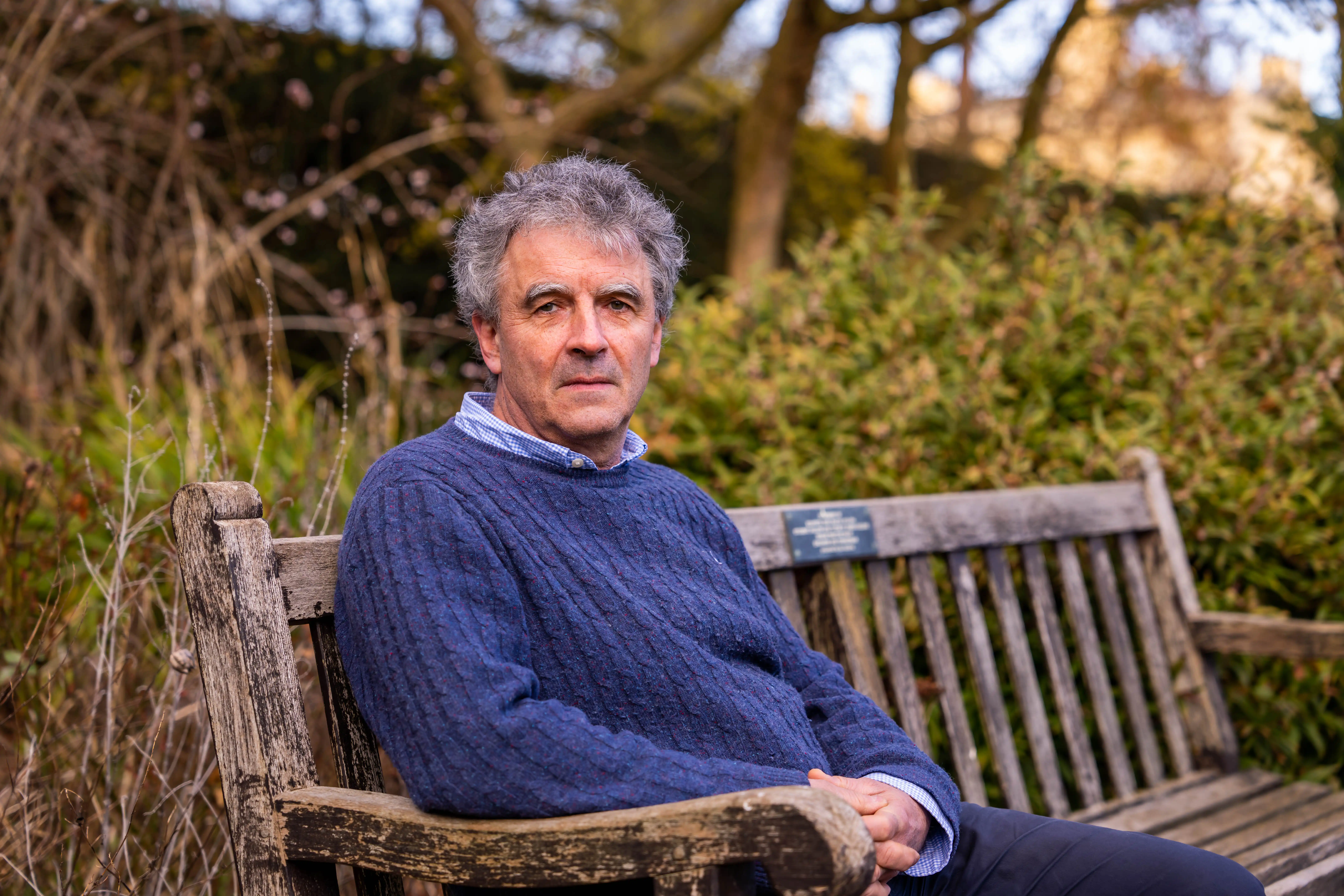 Professor Andrew Woods sits on a bench looking at the camera in the grounds of St John's College, Cambridge