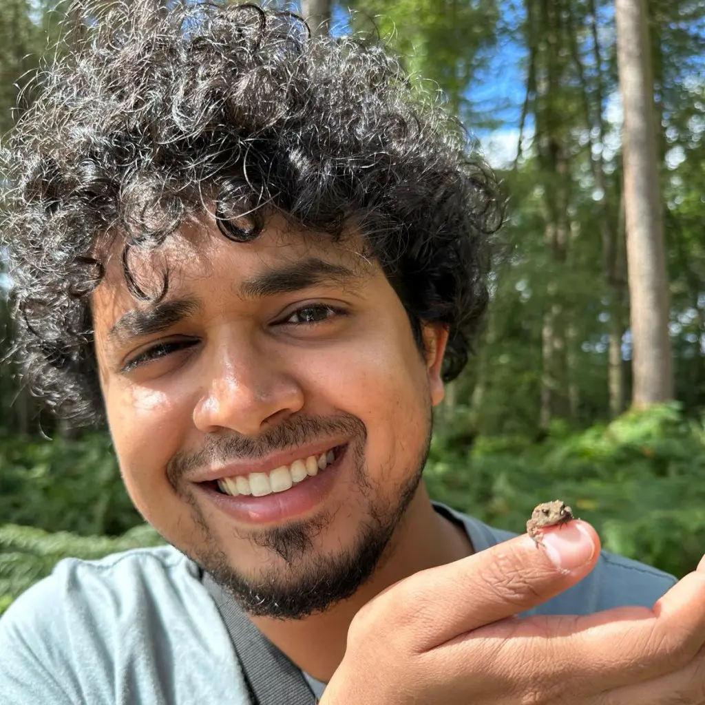 Dr Sonu Kurien smiles at the camera and is holding a tiny frog