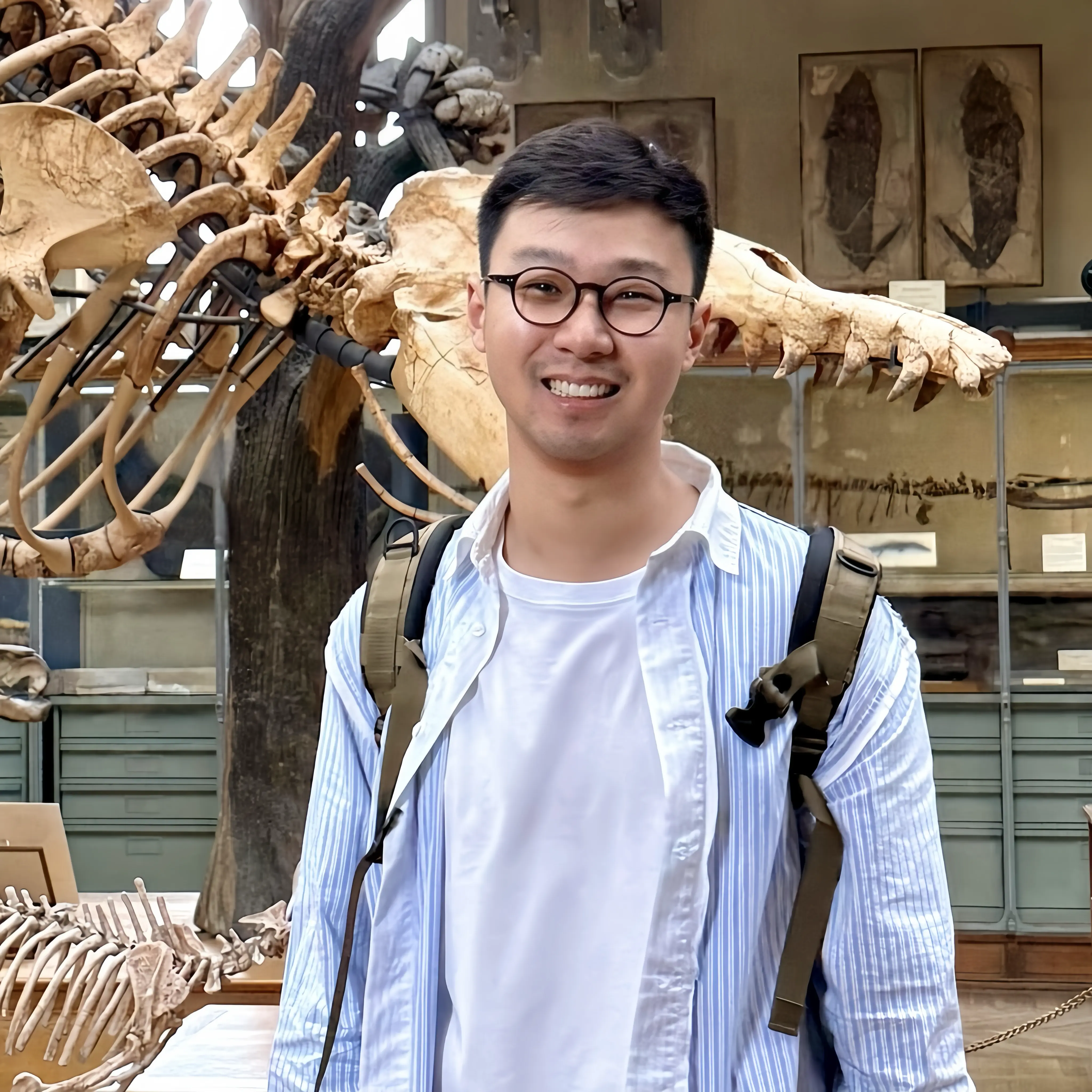 Dr Wang is standing looking at the camera and behind them is a display of animal skeletons