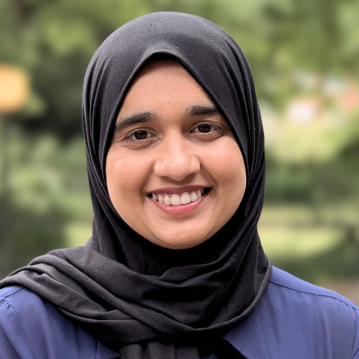 Dr Ashfaq is smiling directly at the camera wearing a navy blue shirt and black hijab scarf