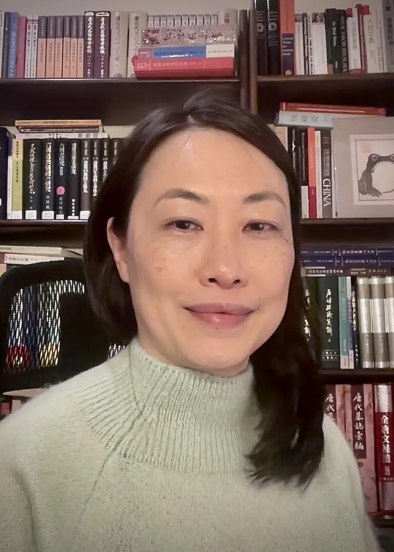 Dr Choo is sitting in front of a book case looking directly at the camera. They are wearing a green knitted jumper. 