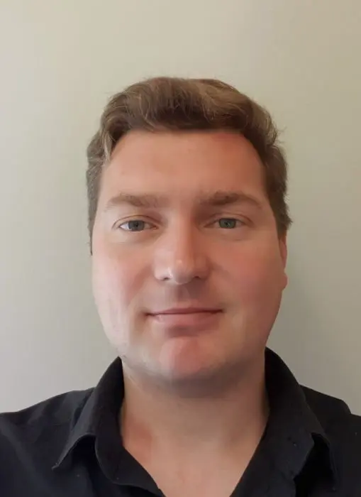 Dr Daniel Ruf is standing in front of a plain wall looking at the camera