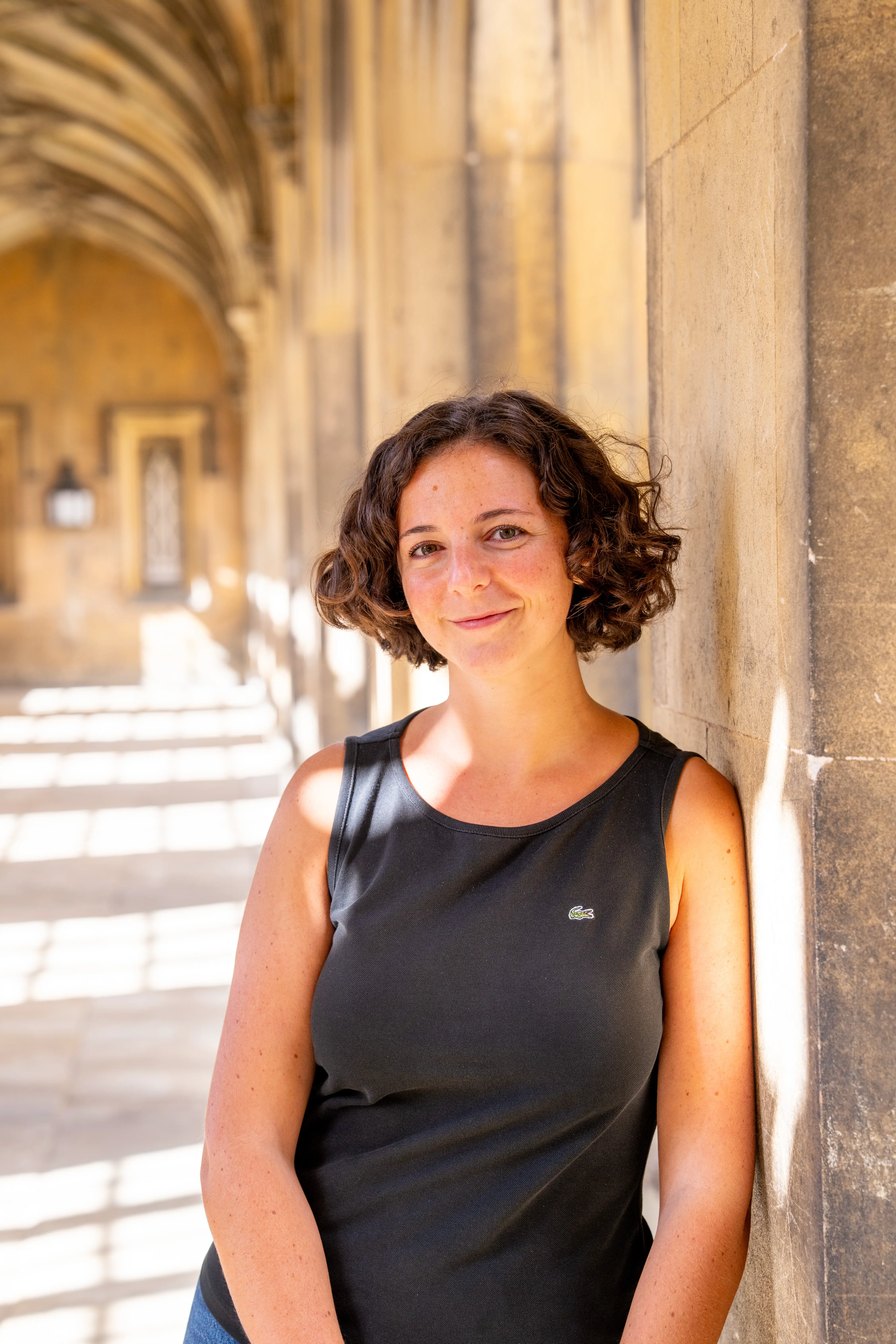 Silvia Marchiori is standing in New Court, leaning on a pillar, looking at the camera