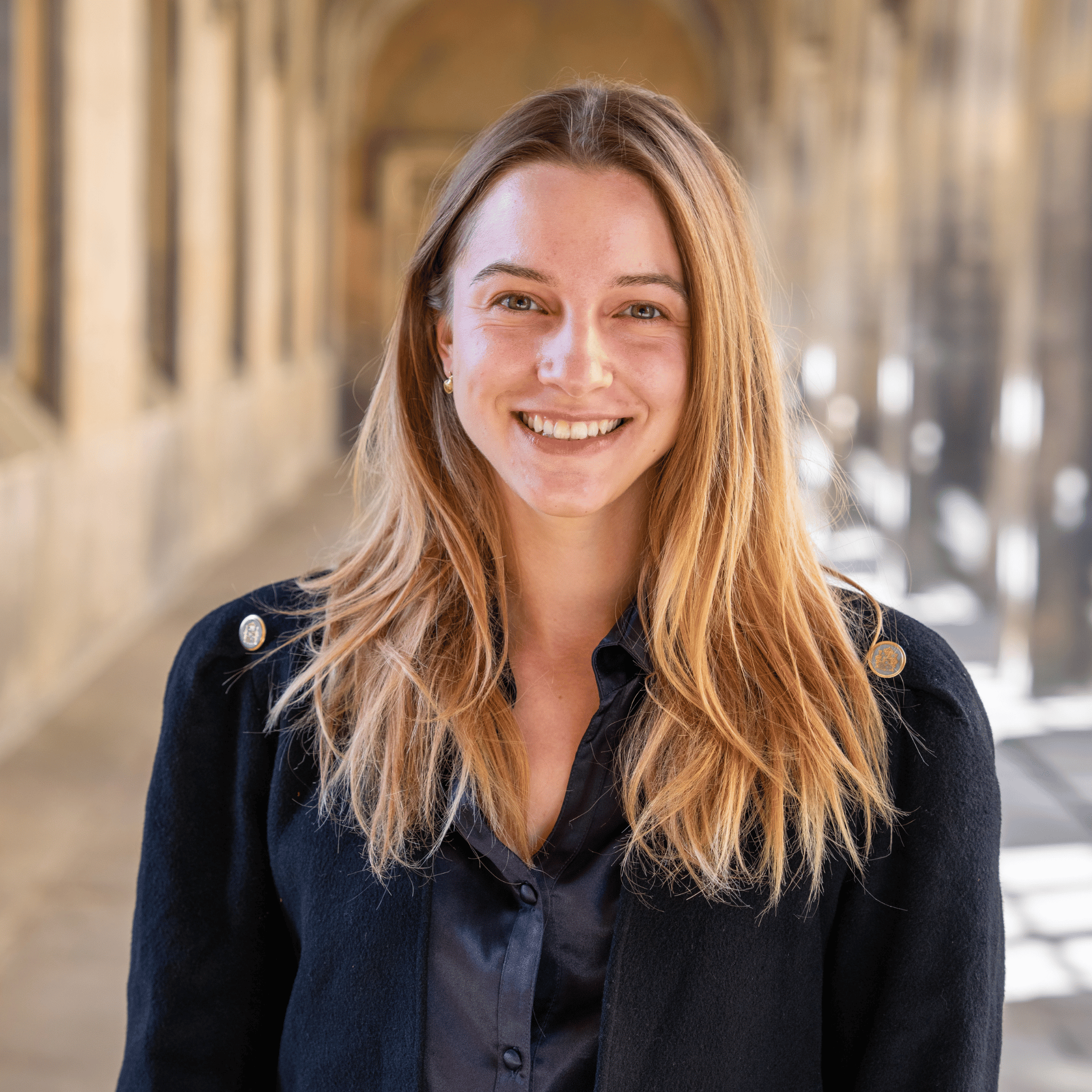 Yara Kyrychenko stands in the cloisters looking into the camera, smiling.