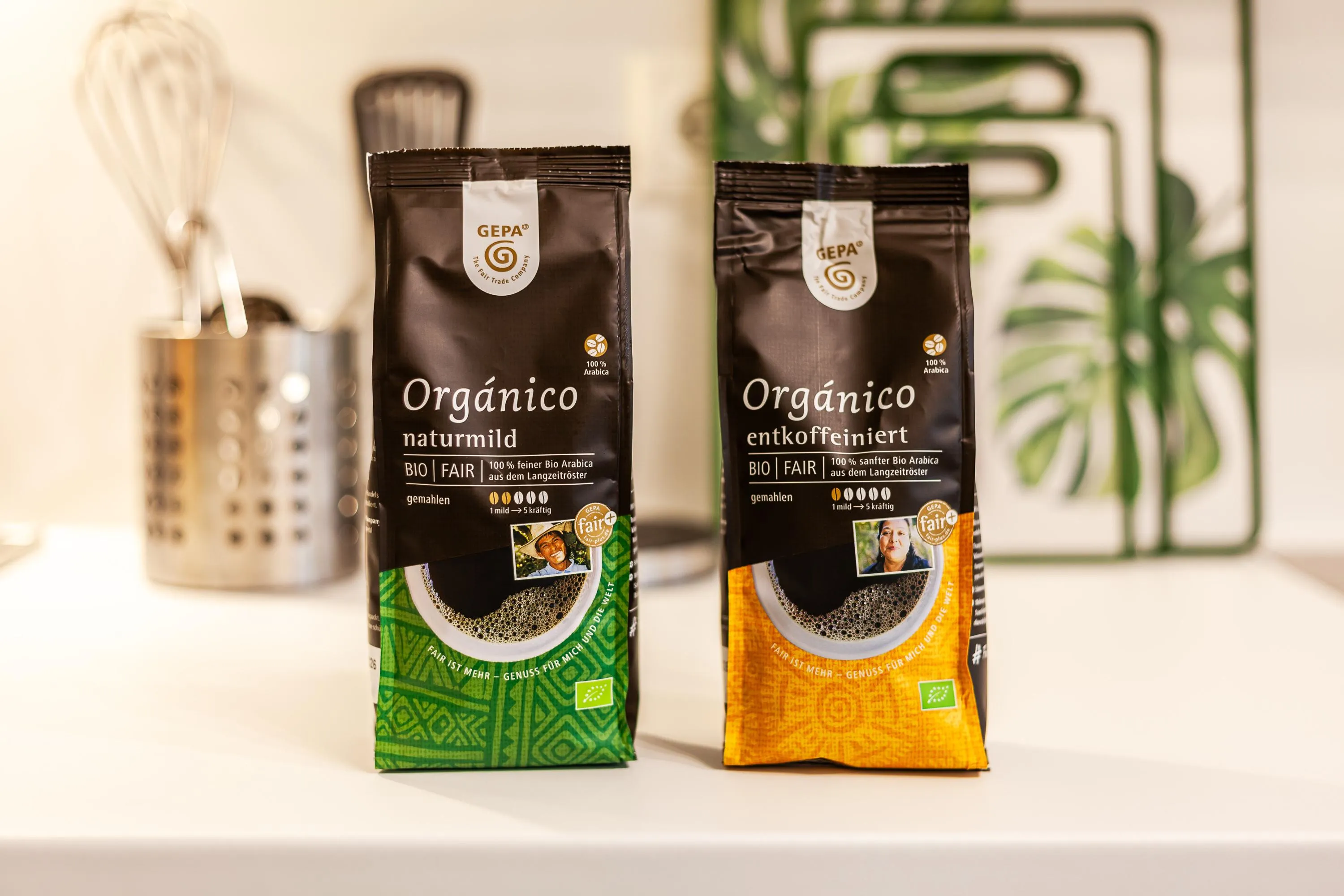 Zwei Packungen GEPA Bio-Kaffee, eine naturmild mit grünem Design, eine entkoffeiniert mit orangefarbenem Design, auf weißer Oberfläche