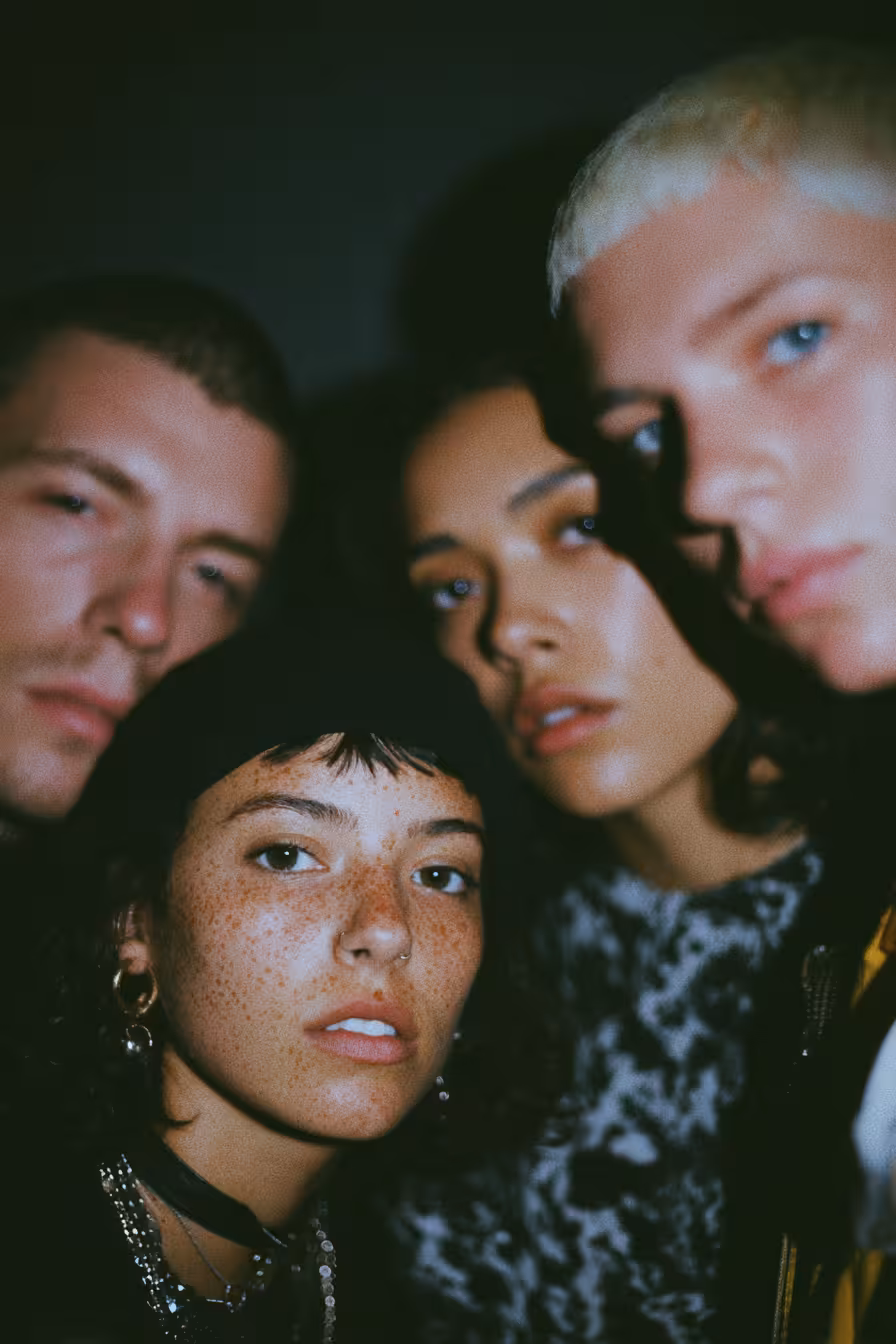 Close-up of four young adults with serious expressions in dim lighting.