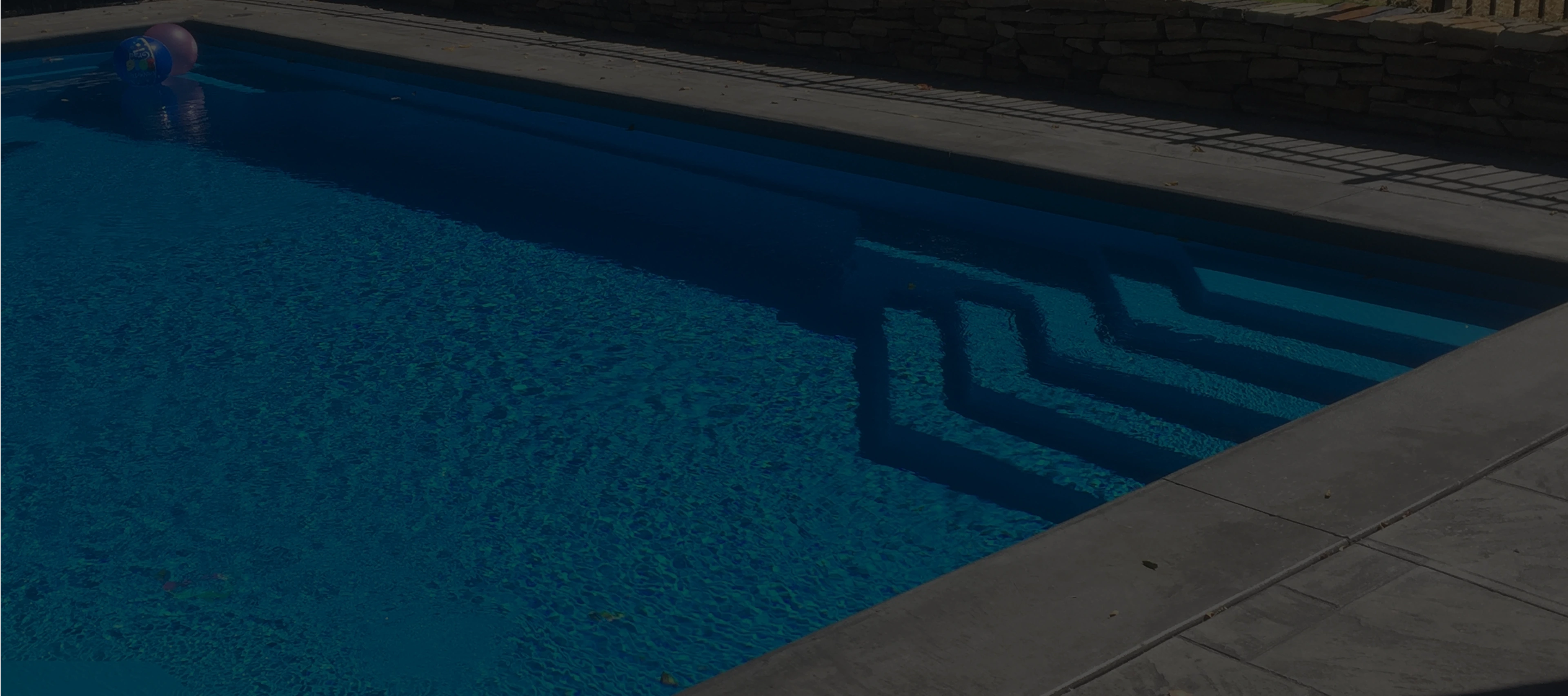 Steps cast shadows in a clear blue outdoor swimming pool, with concrete decking.