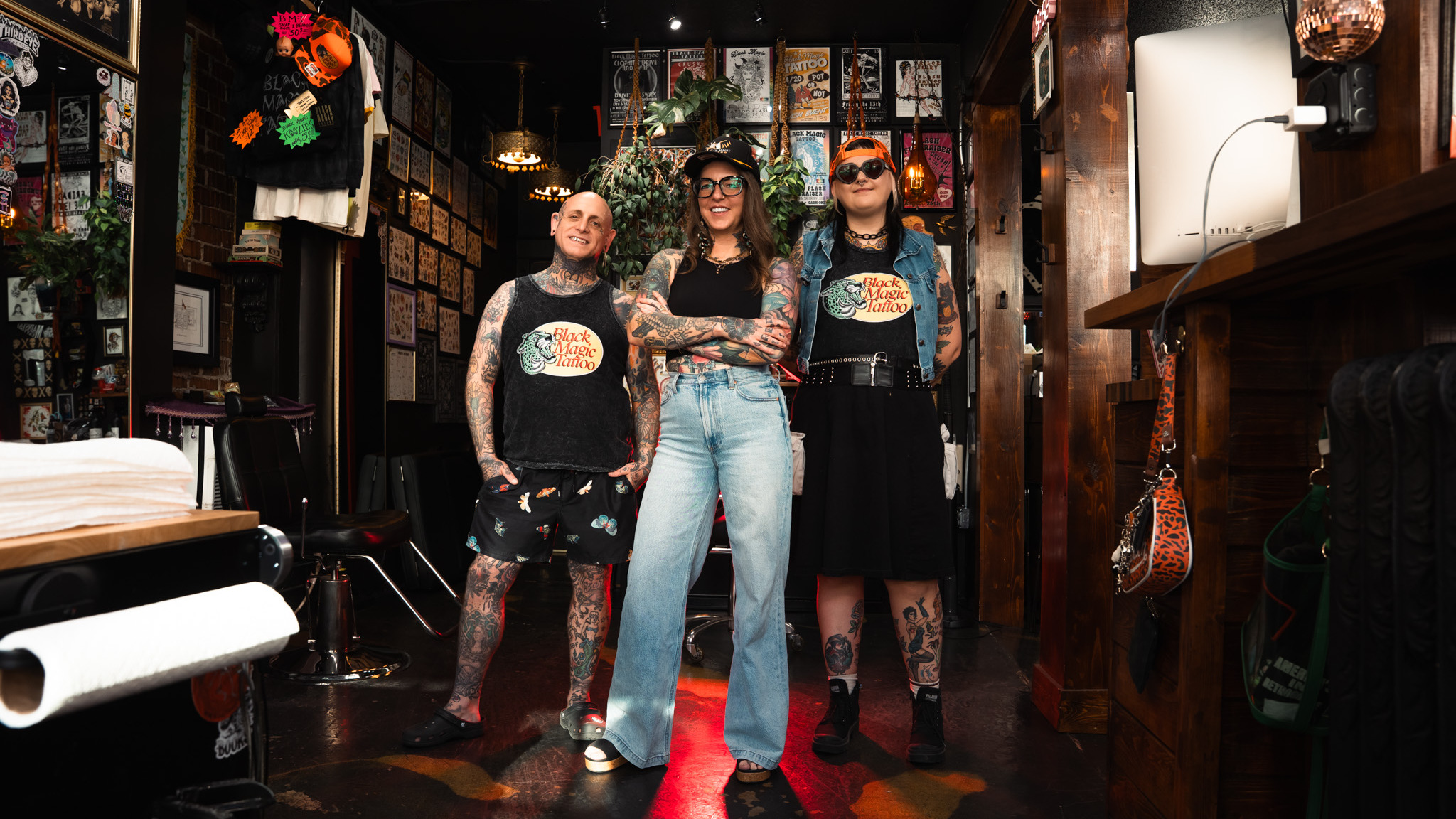 Three tattoo artists in a full tattoo shop interior