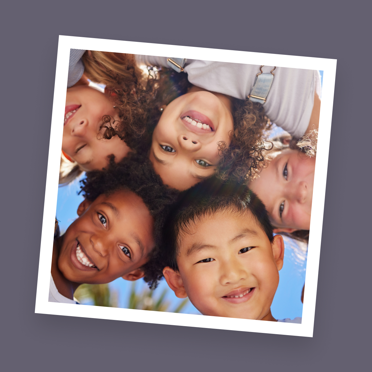 Group of smiling elementary students huddled together looking down at the camera