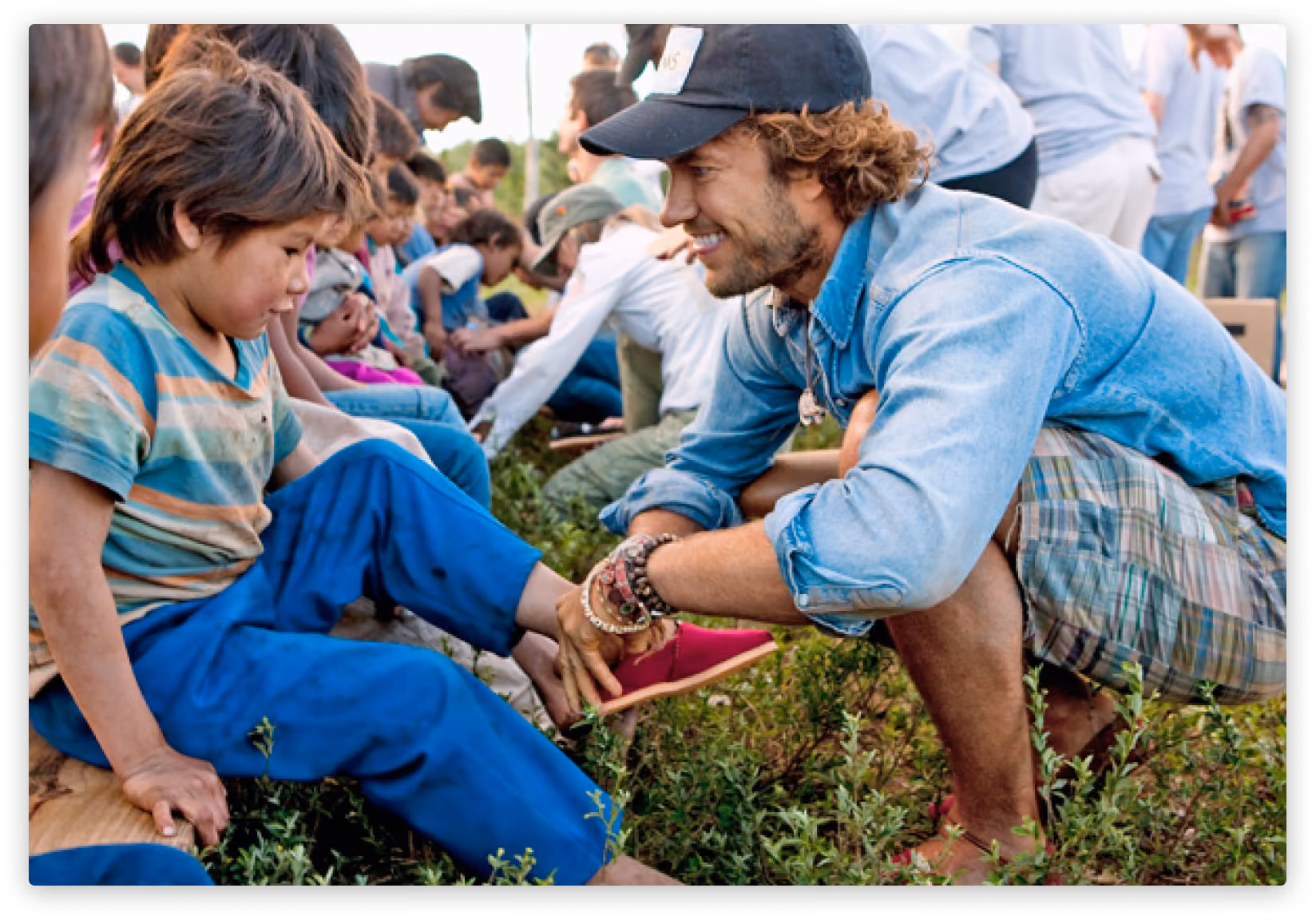 Man putting red TOMS shoes on a little boy