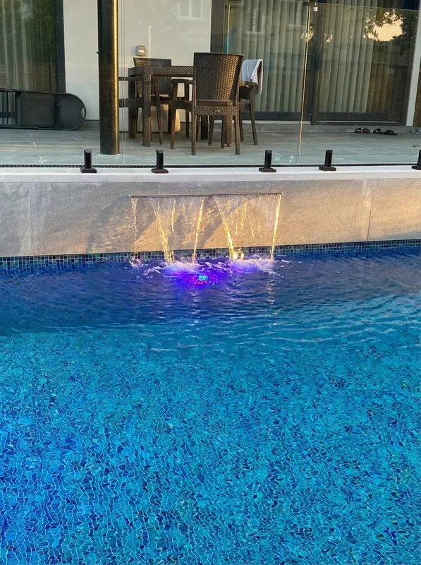 Waterfall feature integrated into deck wall flowing into concrete pool at Wildwood Drive