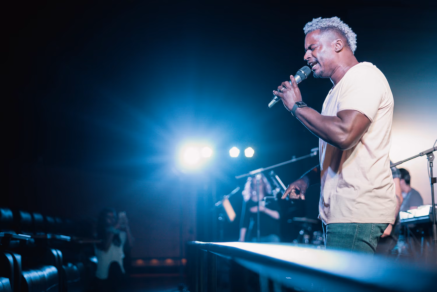 Malik Edwards preaching passionately into a microphone on stage with bright blue stage lights behind him.