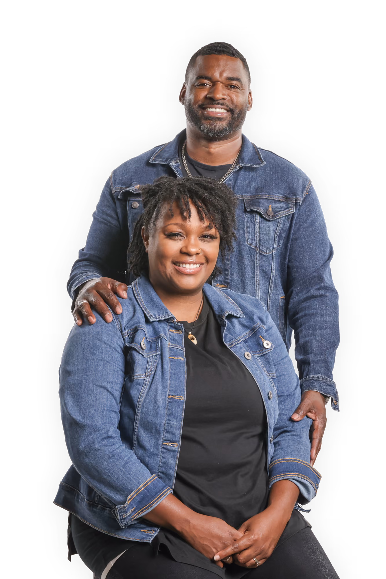 Malik Edwards stands behind seated Ashley Edwards, both wearing denim jackets, against plain background.