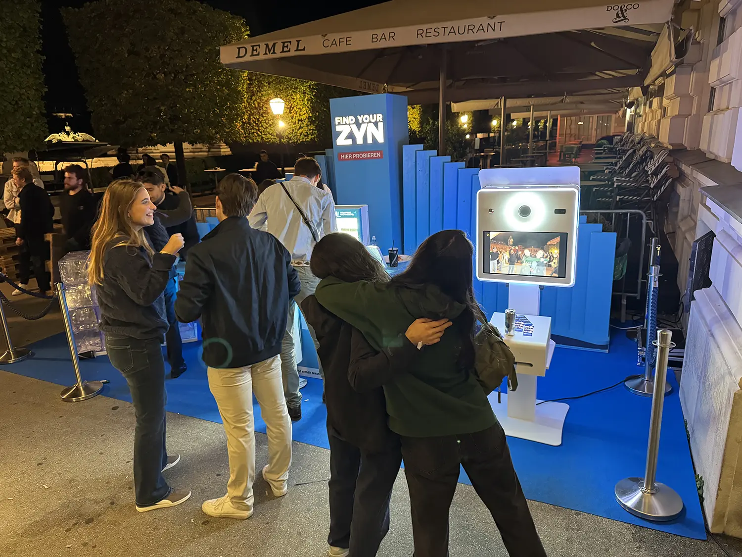 Gäste umarmen sich vor der Fotobox Classic bei einem Markenevent mit blauer Kulisse