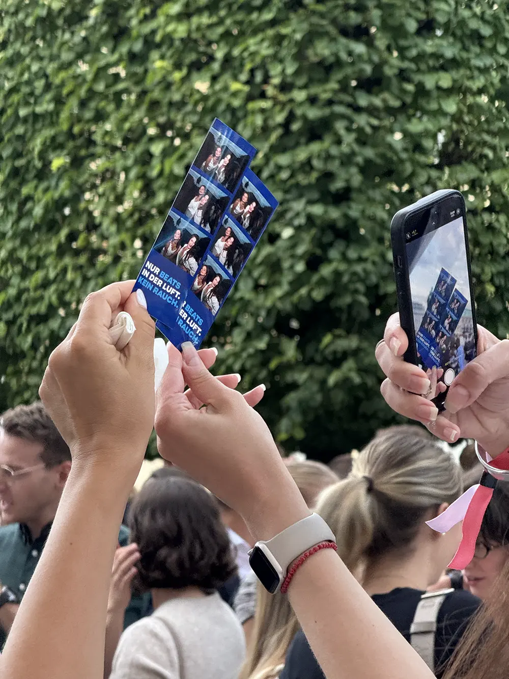 Gäste halten frisch gedruckte Fotostreifen hoch und fotografieren sie mit dem Handy