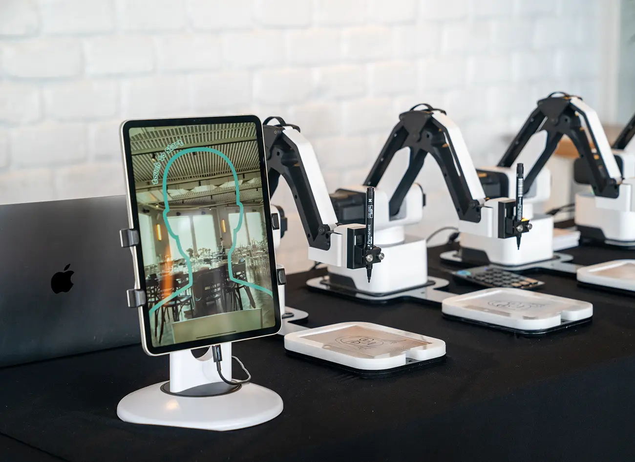 Tablet showing a finished drawing with the AI Sketcher robots behind