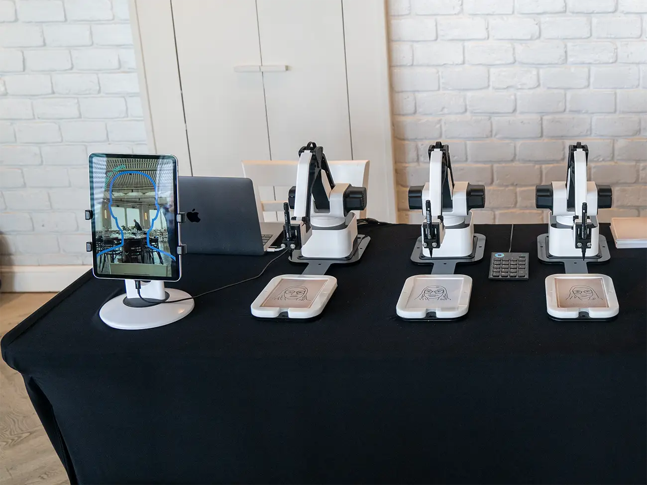 Four AI Sketcher robots on a black table with a preview tablet