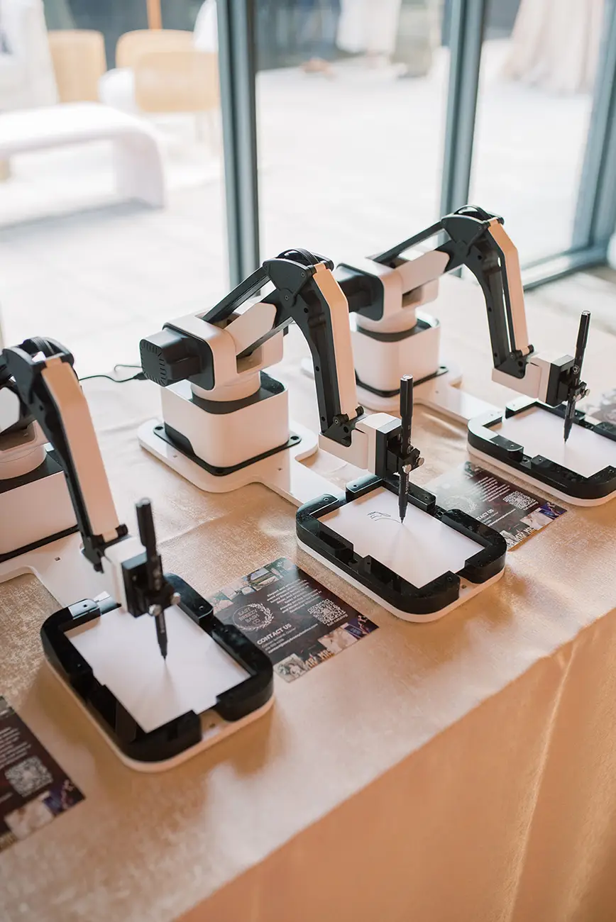 Three AI Sketcher robots on a table in front of a large window