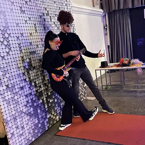 Two guests posing in front of a silver sequin wall at the mirror photo booth
